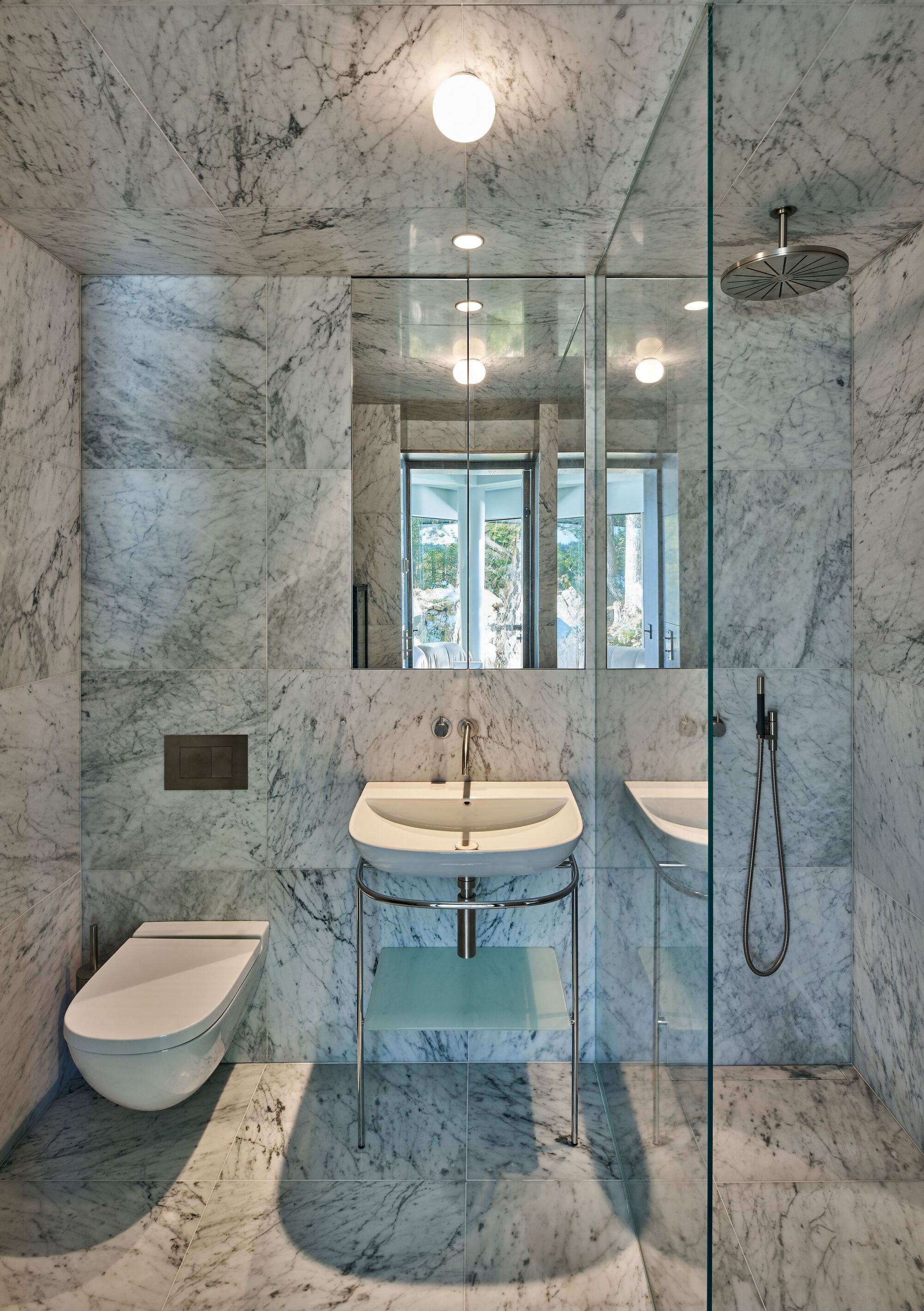 Bathroom clad entirely in white veined marble with glass shower enclosure and globe pendant lights