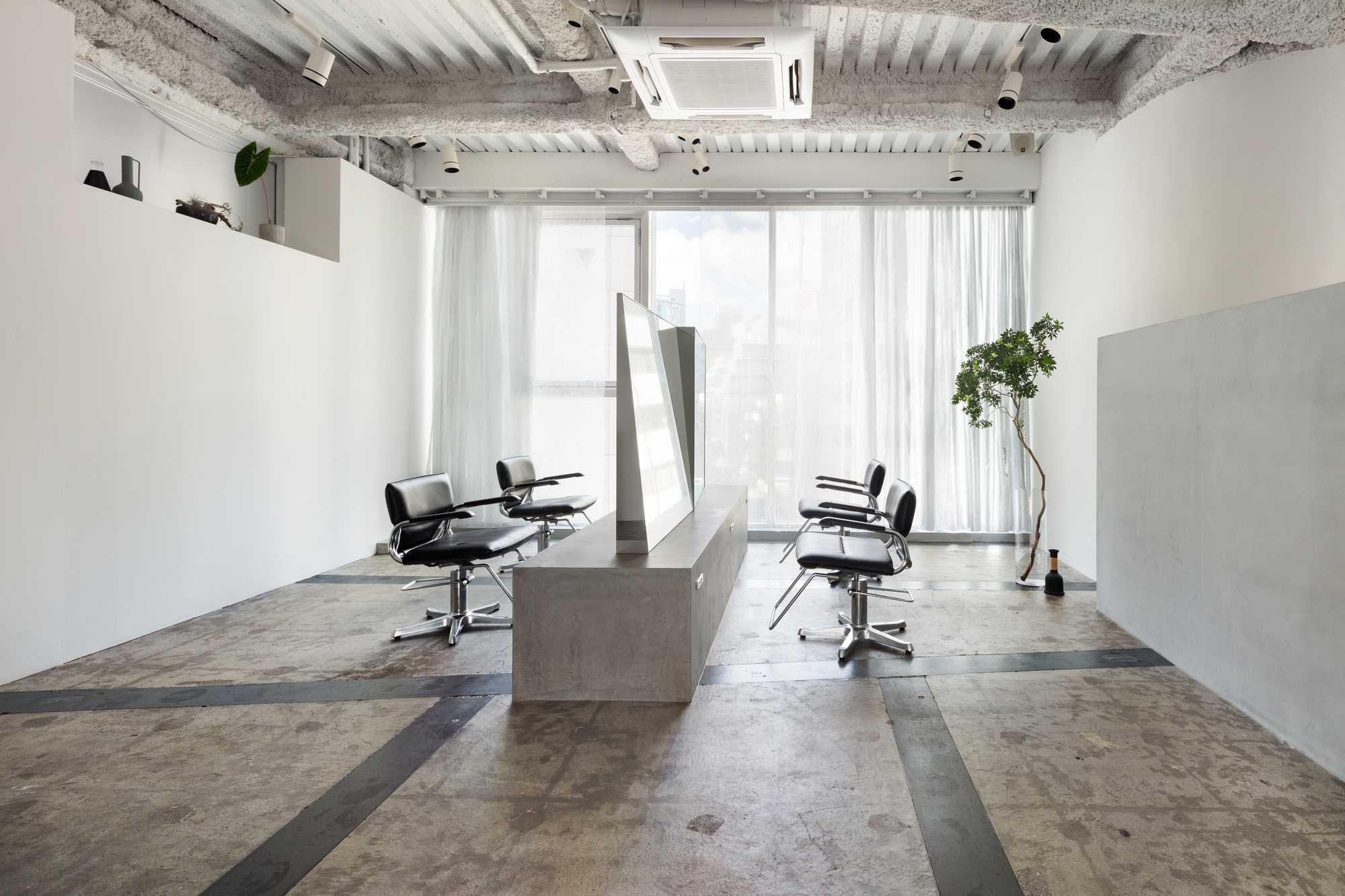 Salon workspace with concrete stations and sheer curtains filtering light from the window wall