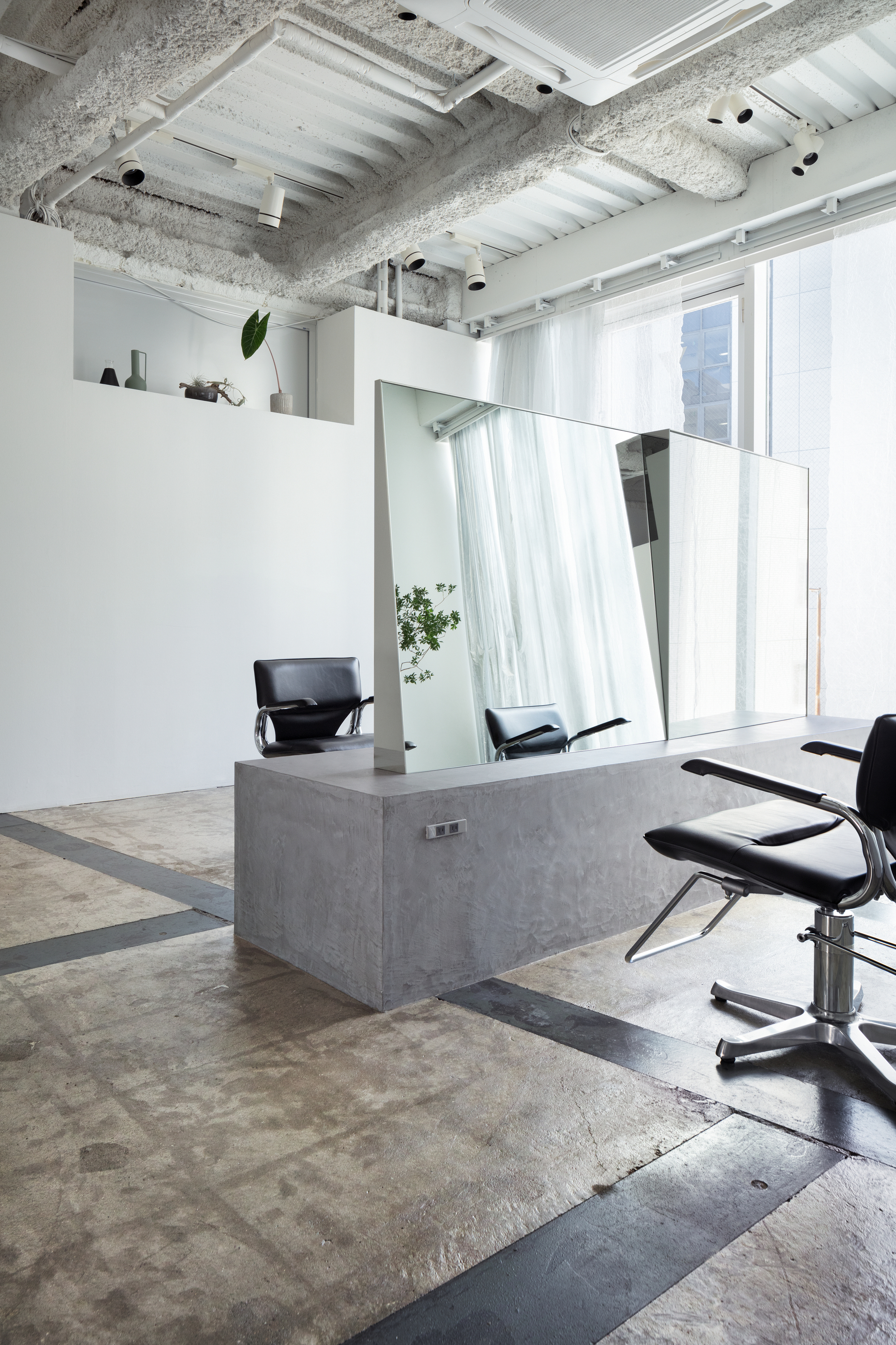 Angled mirror above concrete vanity station reflecting white curtains and natural light