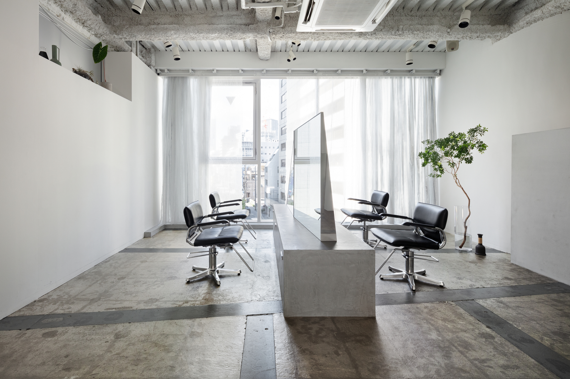 Salon interior with concrete island and floor-to-ceiling windows overlooking adjacent buildings