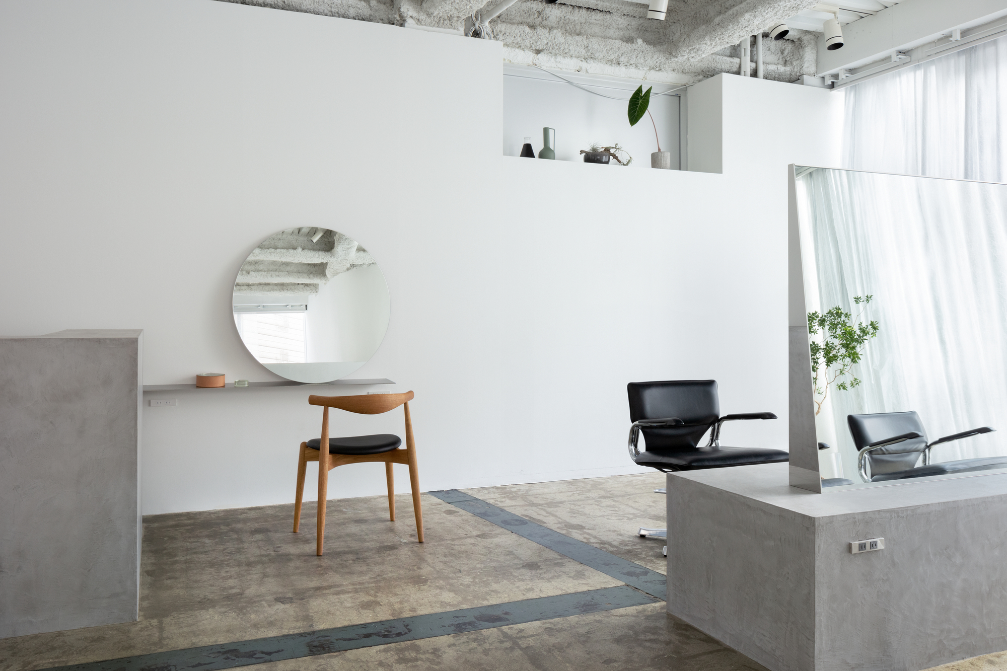 Workspace corner with circular mirror, wooden chair, and concrete desk beneath an exposed concrete ceiling