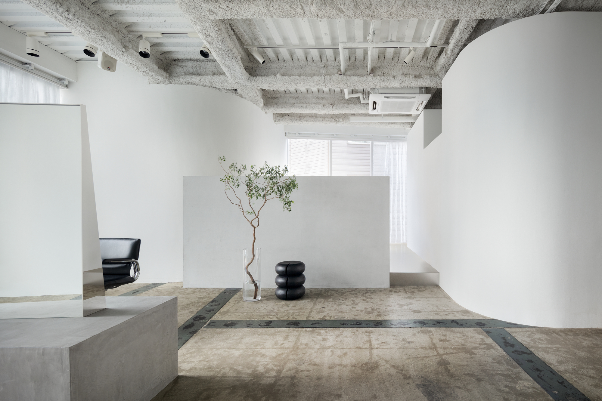 Open salon floor with curved white volume, concrete platforms, and slender tree beside sheer curtains