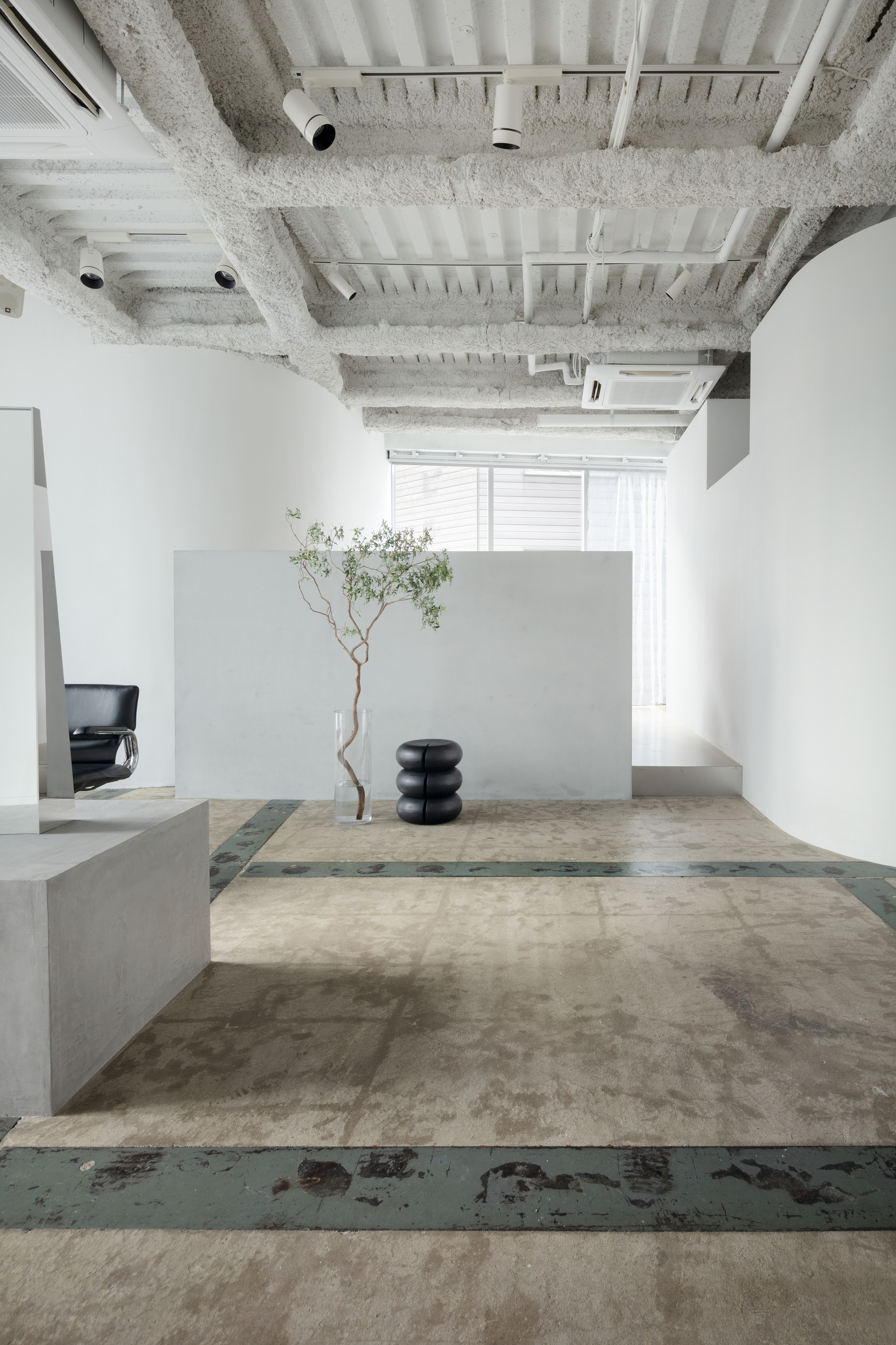 Salon platforms with layered concrete surfaces, decorative tree, and exposed ribbed ceiling with mechanical systems