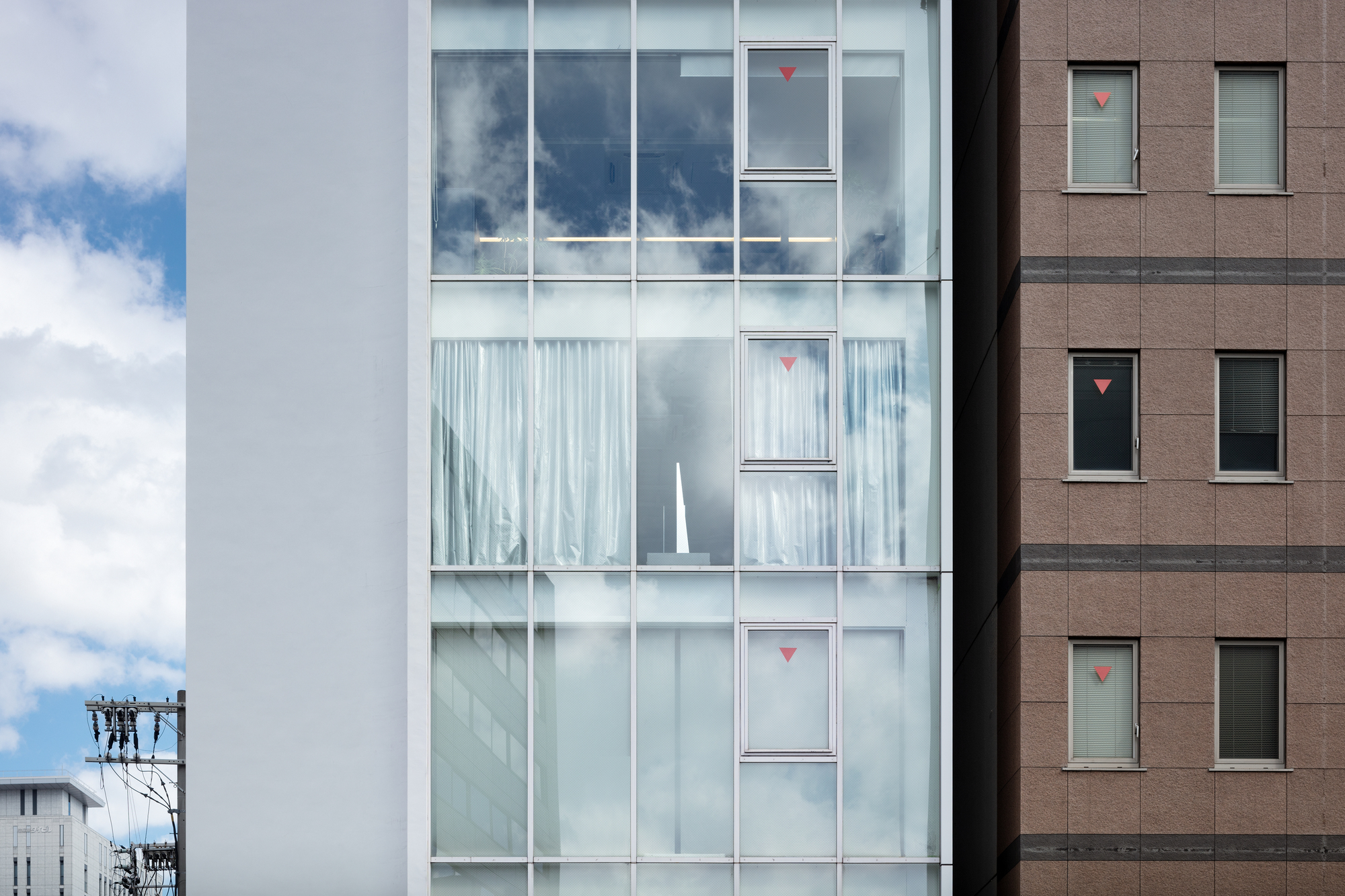 Close view of the glazed facade showing floor-to-ceiling windows with sheer curtains and red signage