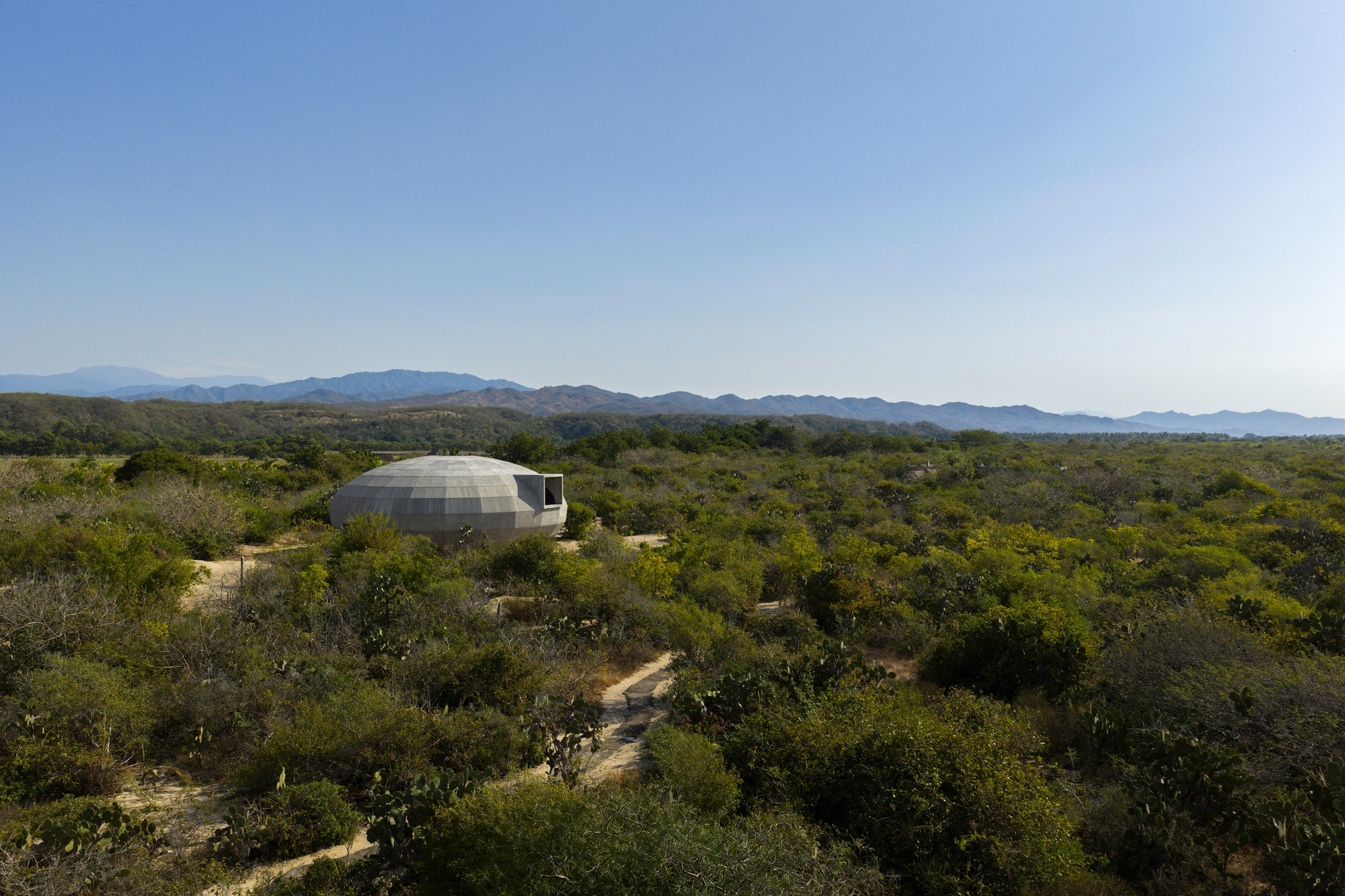 Domed concrete structure nestled in arid landscape with distant mountain ranges under clear sky