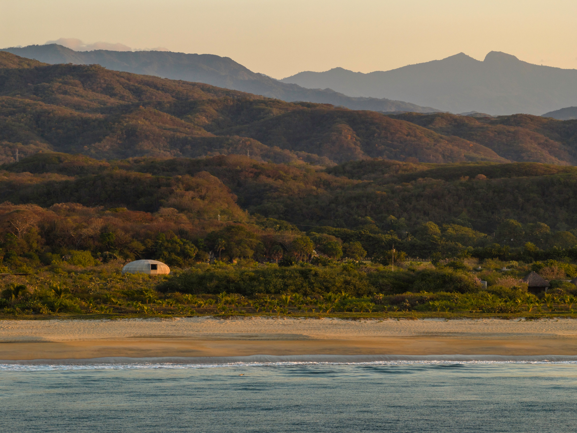 Distant view of the dome from the beach at golden hour with layered mountains beyond