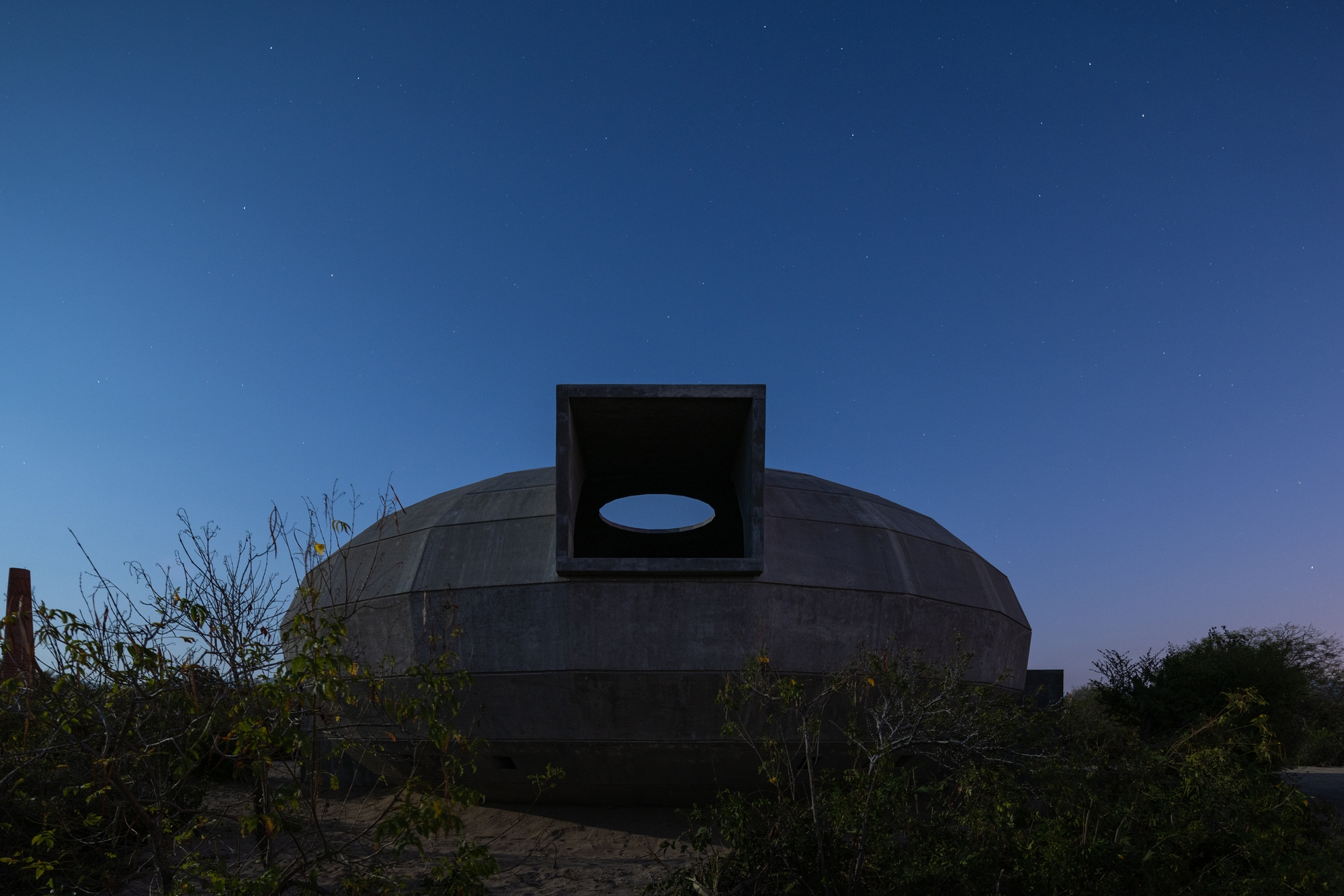 Concrete dome with a central chimney opening framed by an oval oculus at dusk