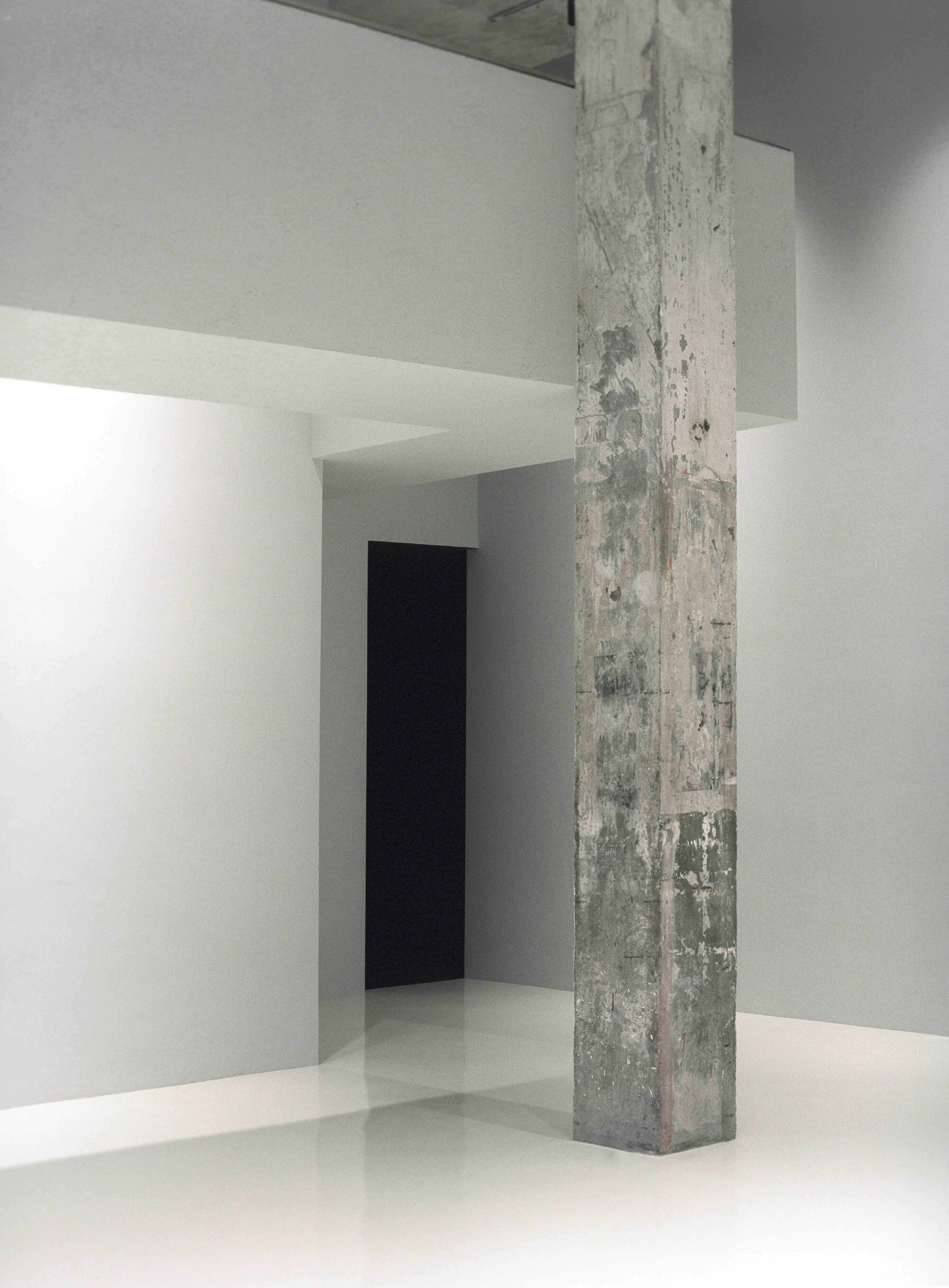 Exposed concrete column standing in a white gallery space with smooth resin flooring