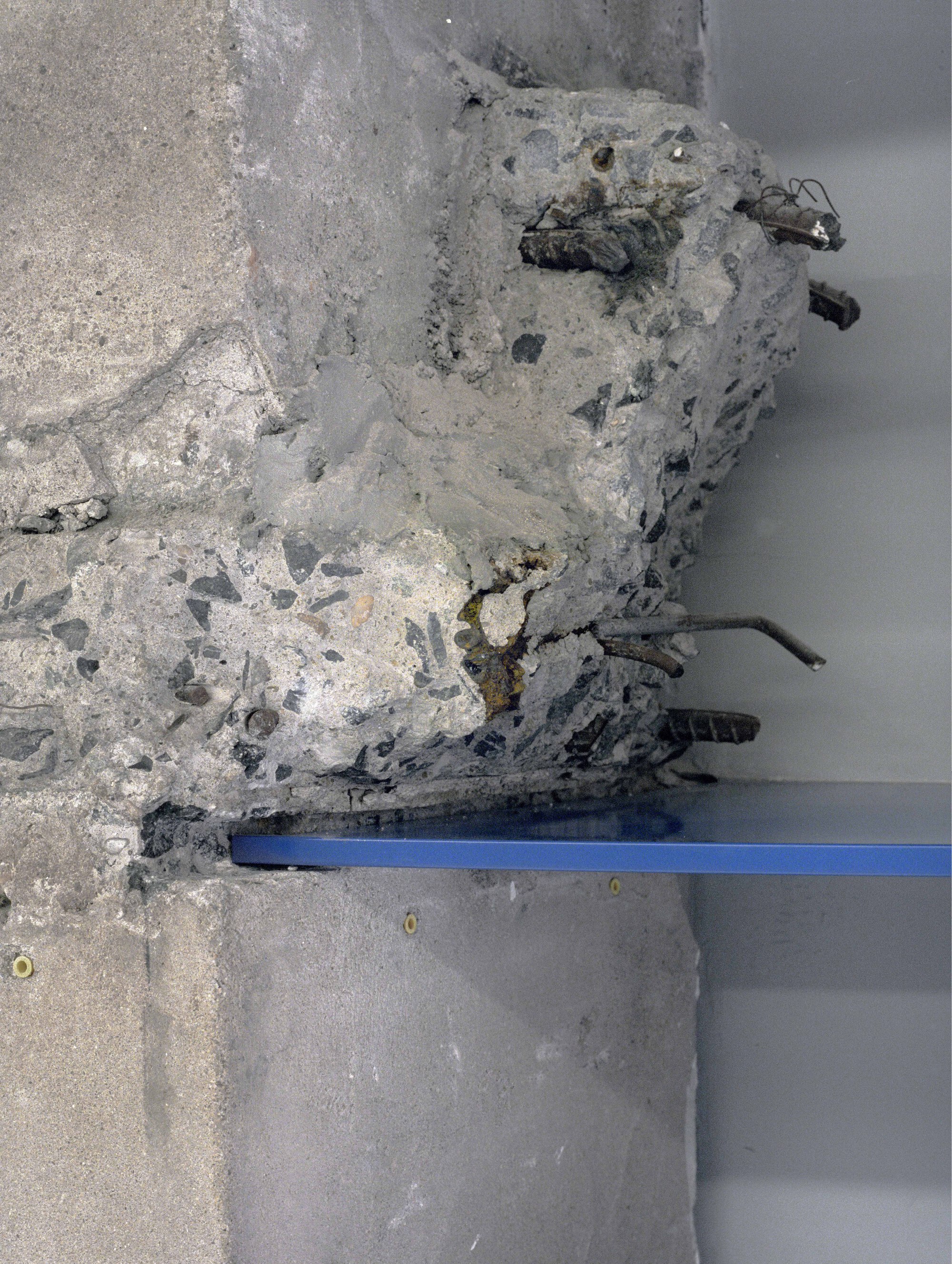 Close-up detail of deteriorated concrete with exposed aggregate and embedded metal reinforcement bars