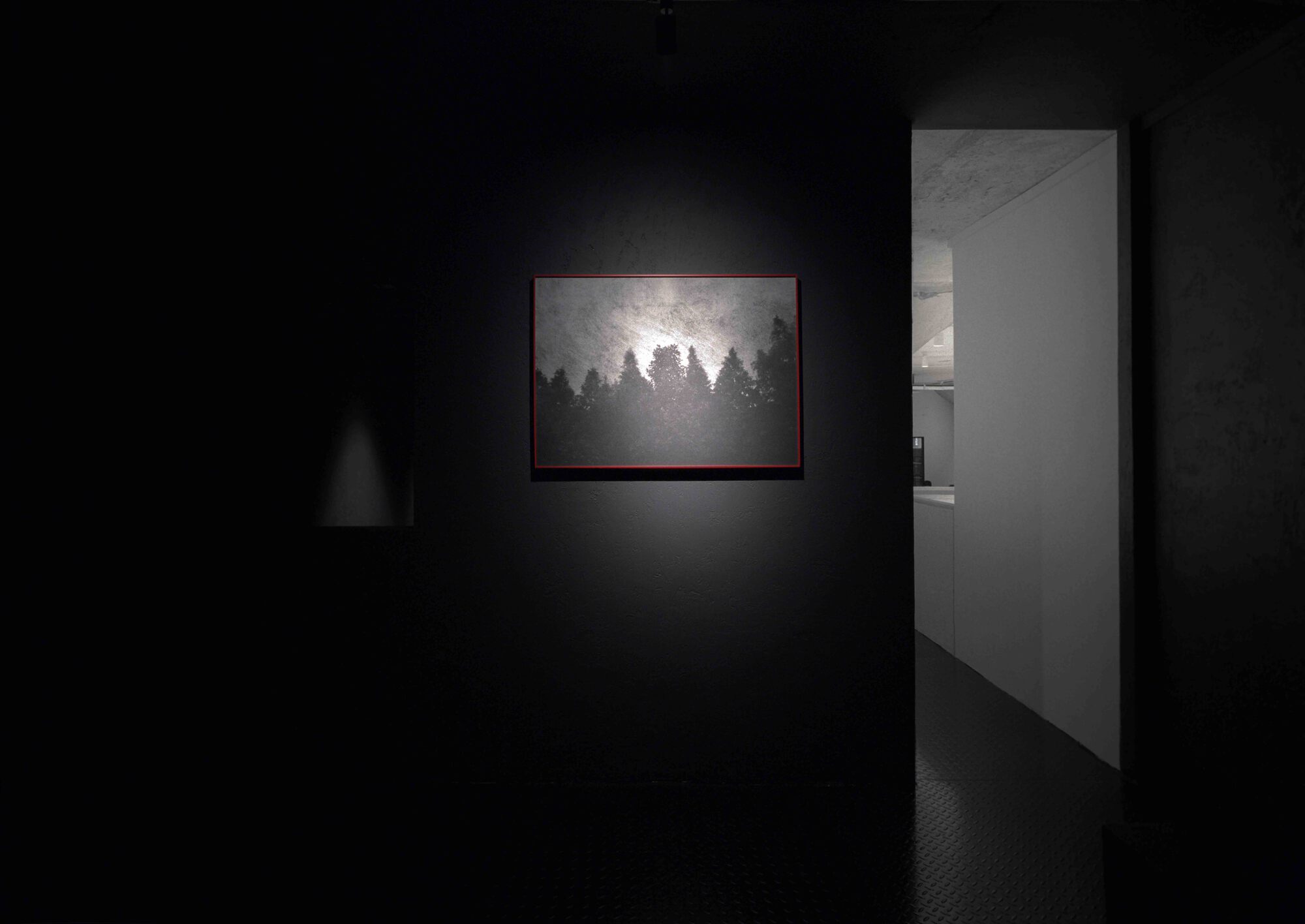 Gallery room with black walls and a single illuminated artwork beside an open doorway