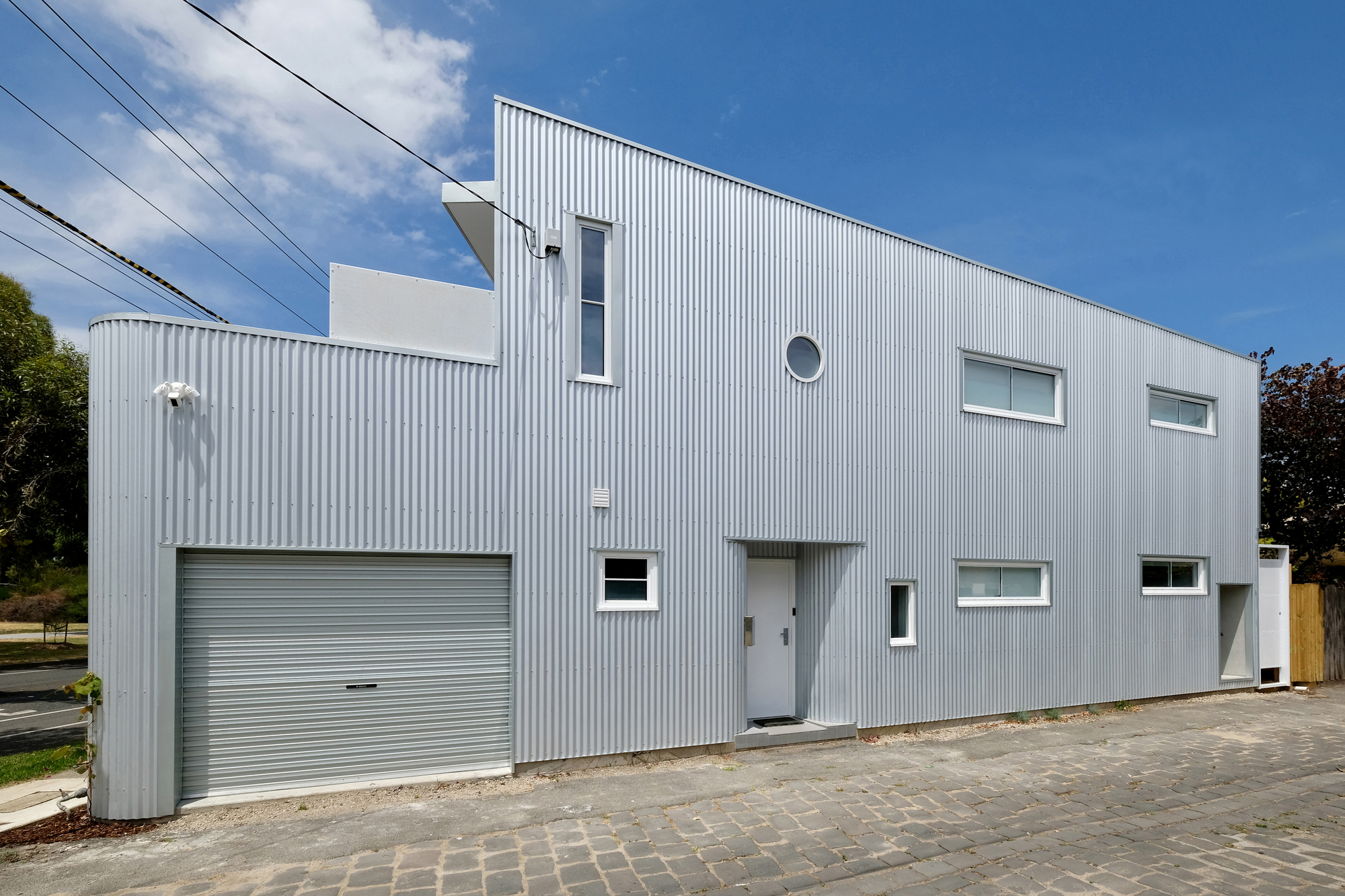Street view of the white corrugated metal facade with scattered windows and a roll-up garage door