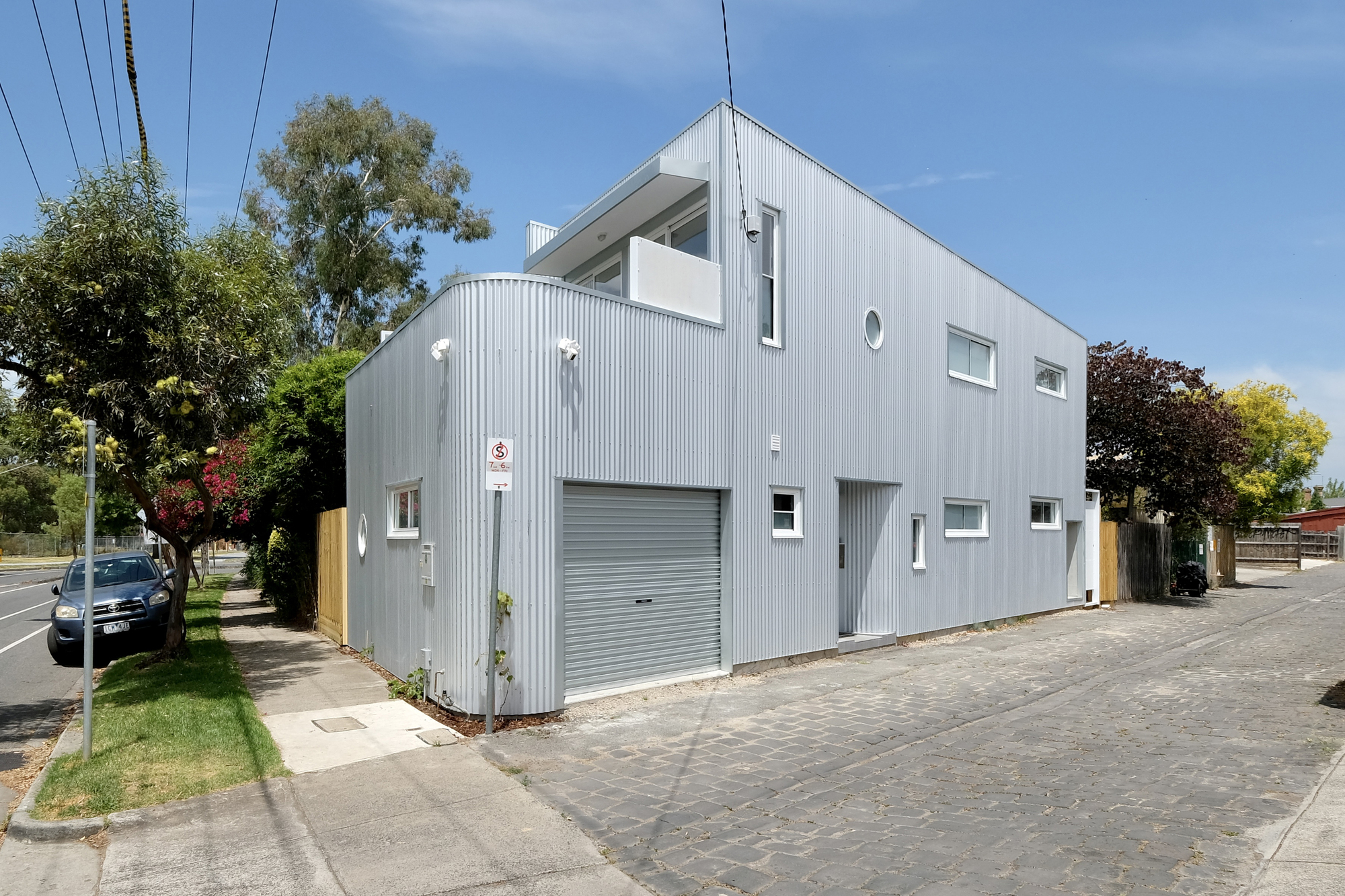 Corner view showing the corrugated metal cladding and garage door from the cobblestone driveway
