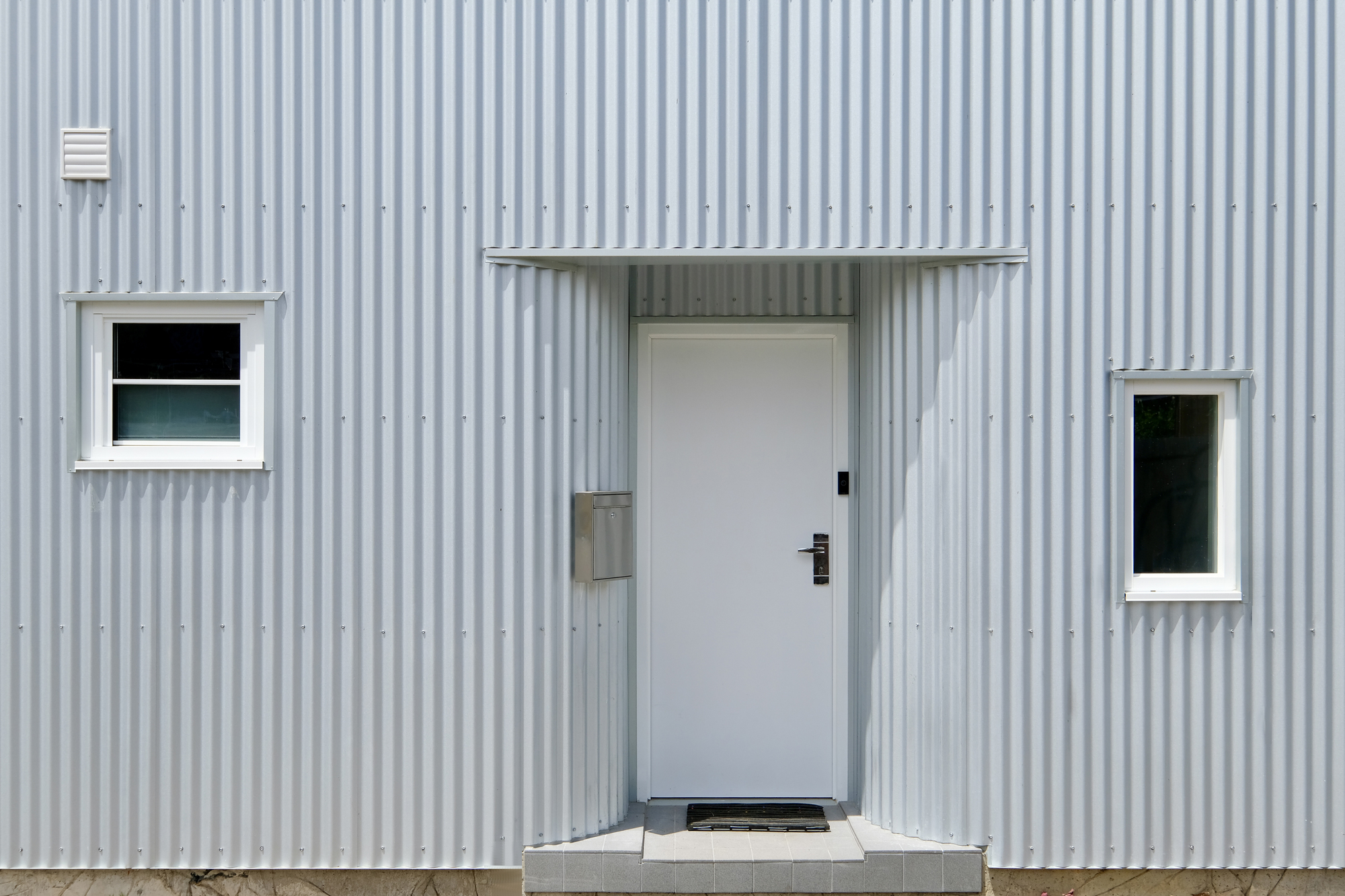 Close-up of the entry door flanked by two square windows on the ribbed metal wall