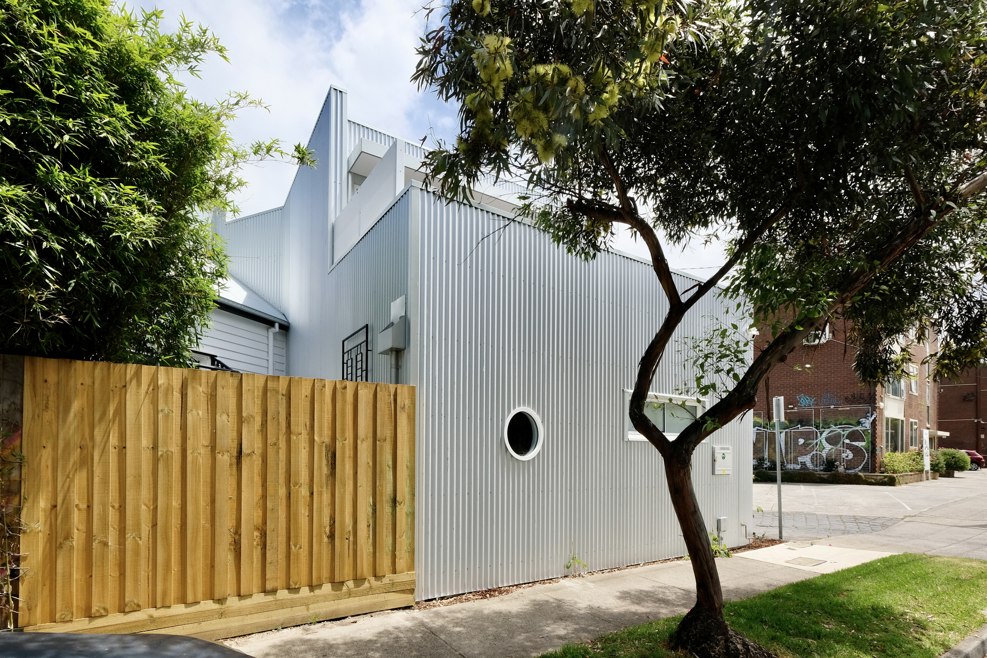 Rear view showing the corrugated facade behind a timber fence and an overhanging eucalyptus tree