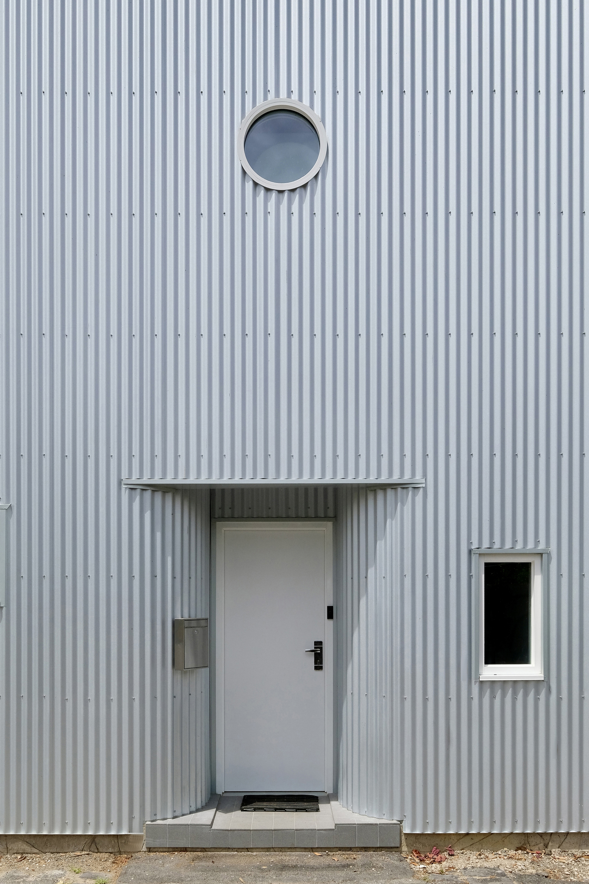 Entry door with canopy and circular porthole window set in the ribbed metal wall
