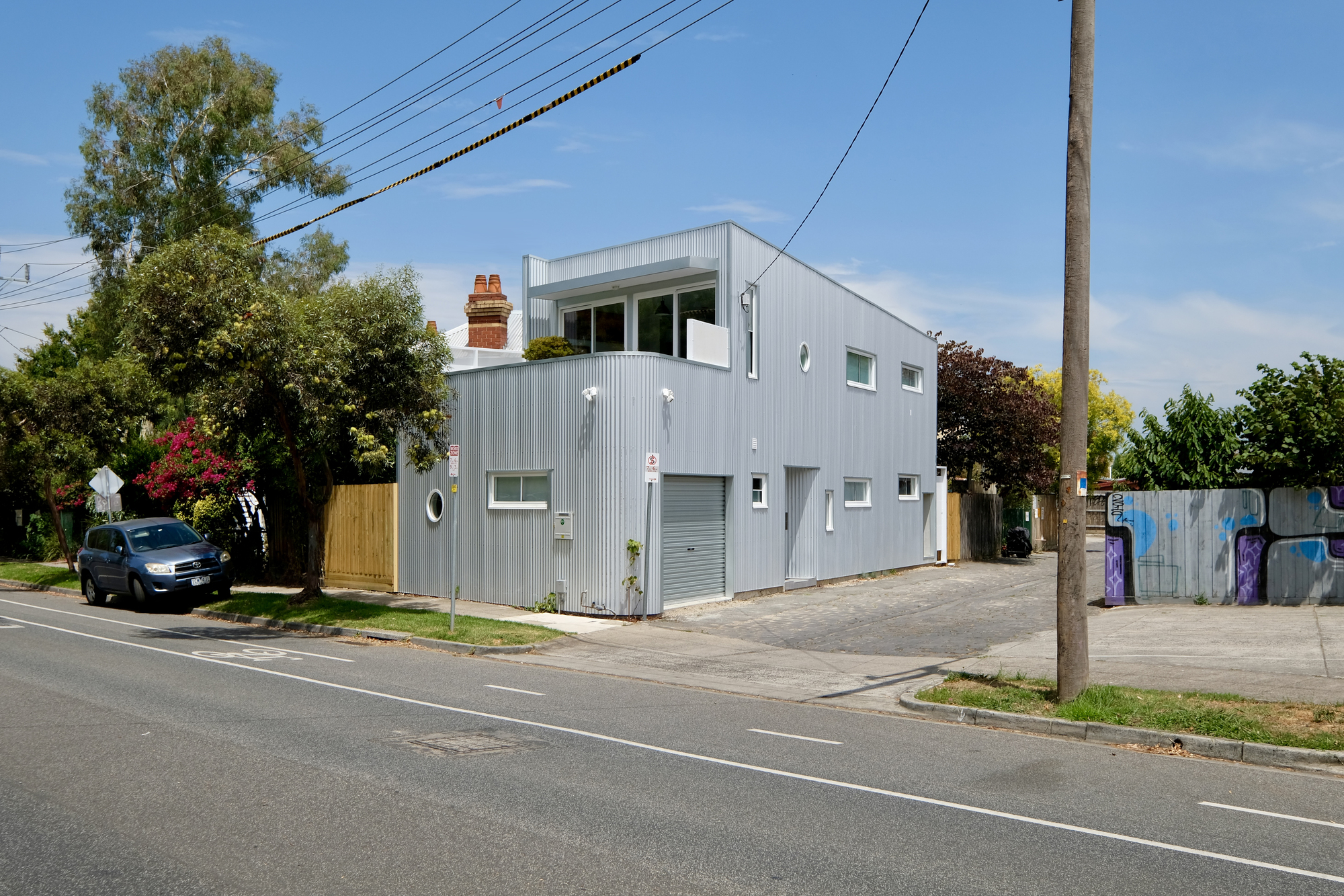 Street view of the two-storey corrugated metal volume with rooftop terrace and chimney