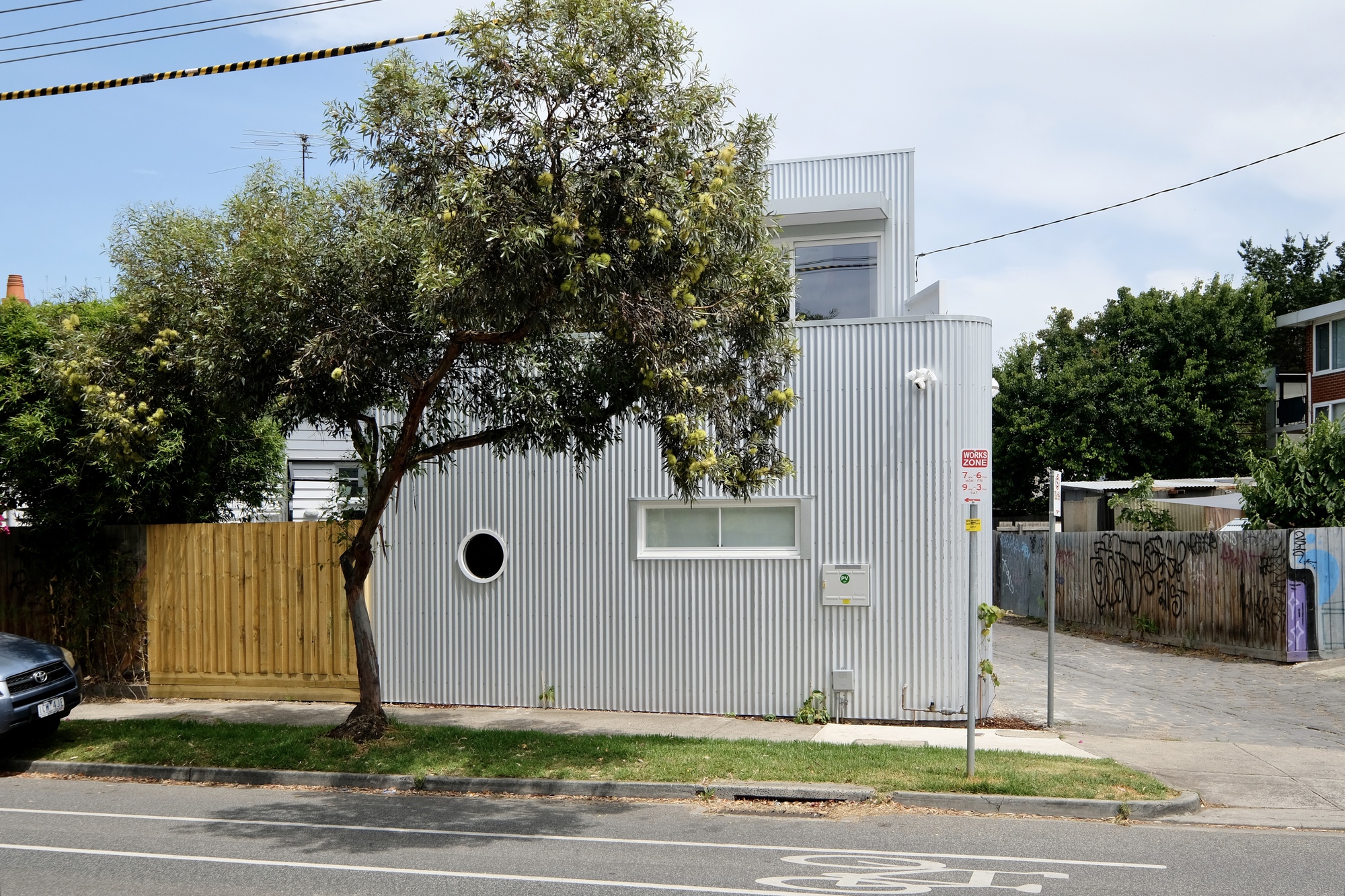 Side facade with circular window and horizontal slot opening beside a mature tree