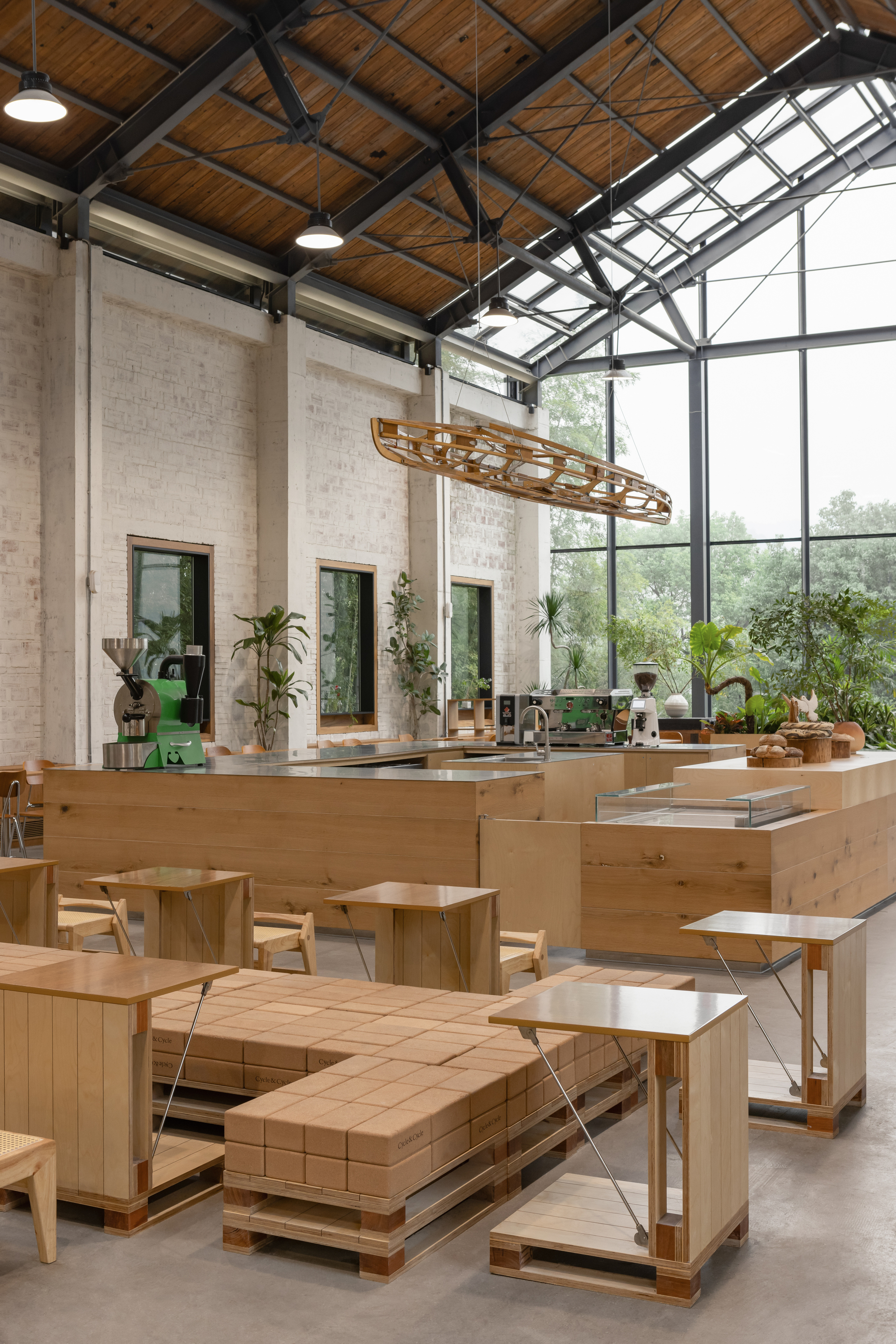Dining hall with glazed gable end, timber service counter and sculptural pendant light suspended from exposed trusses