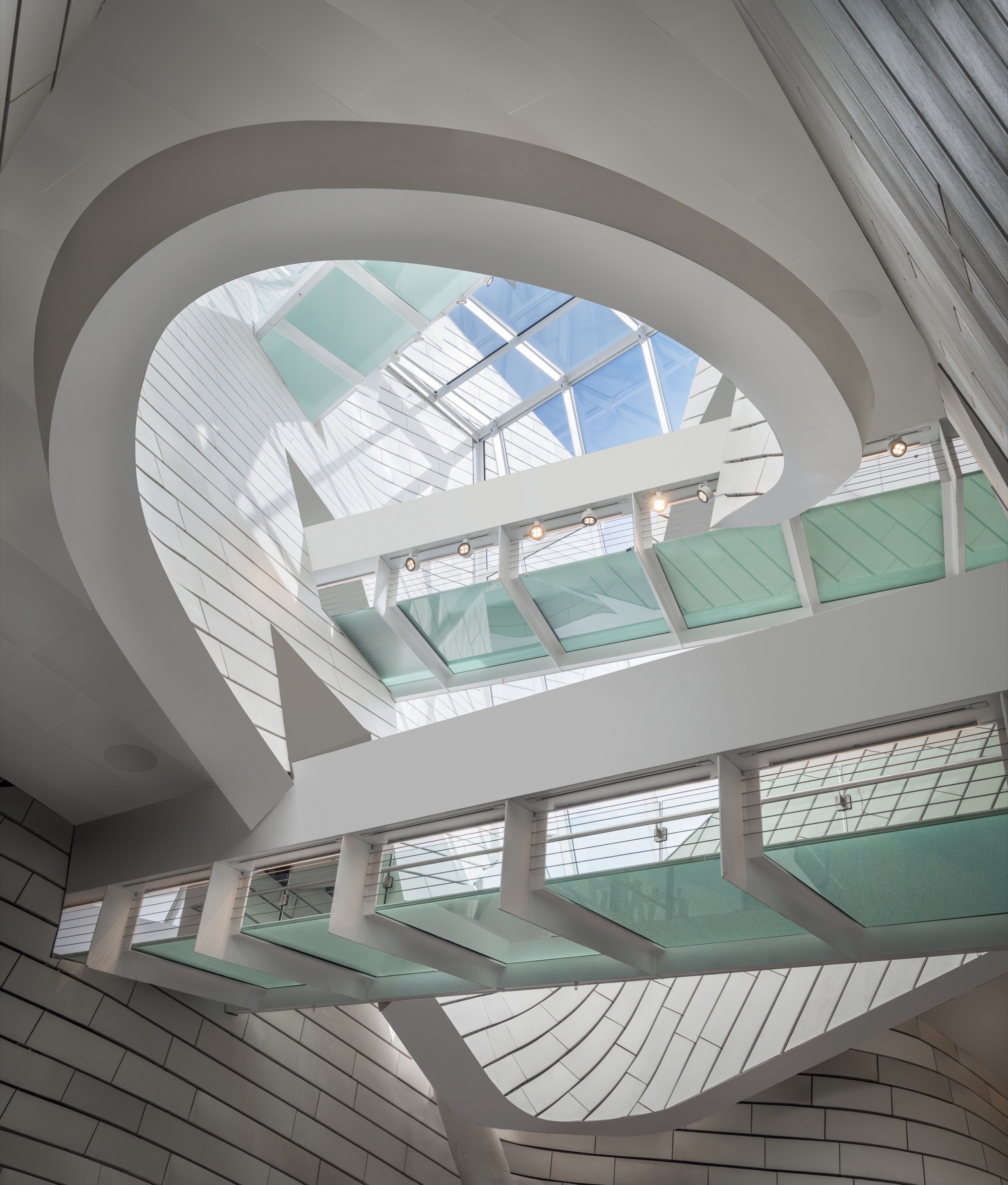 Interior atrium with spiraling white balconies, glass bridges, and skylight flooding the space with daylight