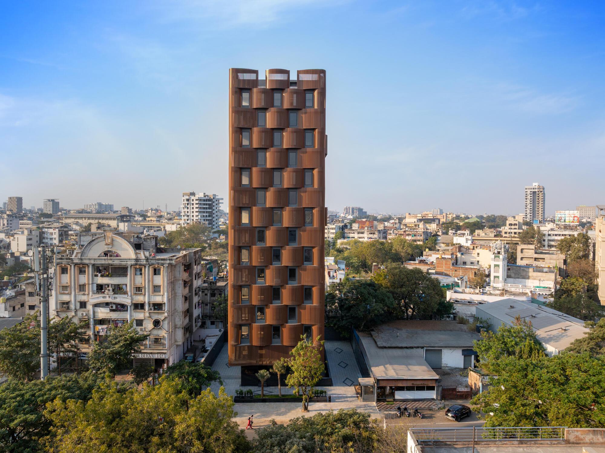 Aerial view of the ribbed terracotta facade tower rising above a dense urban neighborhood with trees