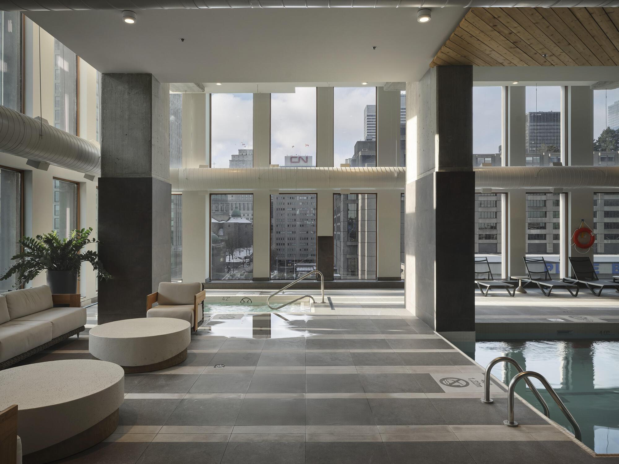 Double-height indoor pool area with concrete columns, wood ceiling and floor-to-ceiling glazing