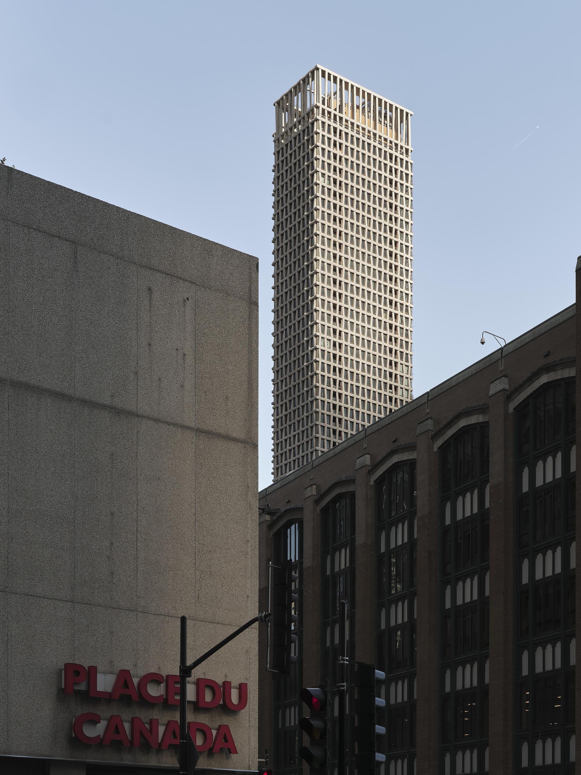 Tower rising behind low-rise concrete buildings and an arched facade in adjacent block