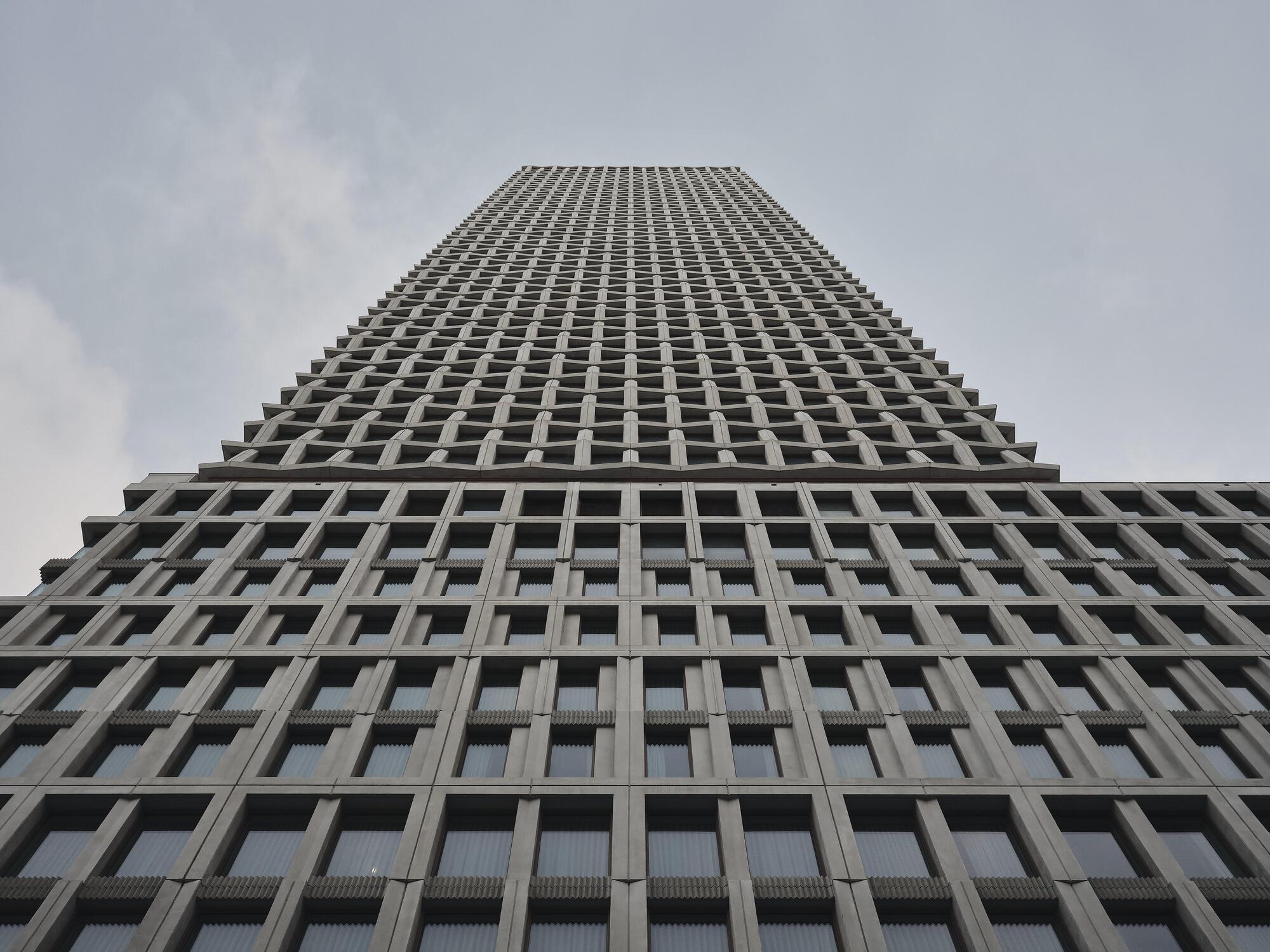 Upward view of the concrete grid facade tapering toward the sky in diffused daylight