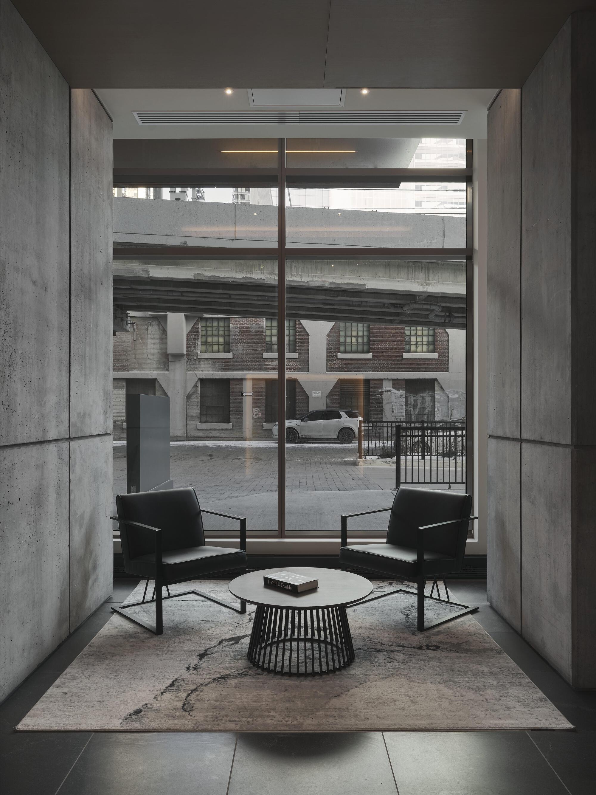 Lobby seating nook with concrete walls and floor-to-ceiling glazing overlooking a courtyard with brick buildings