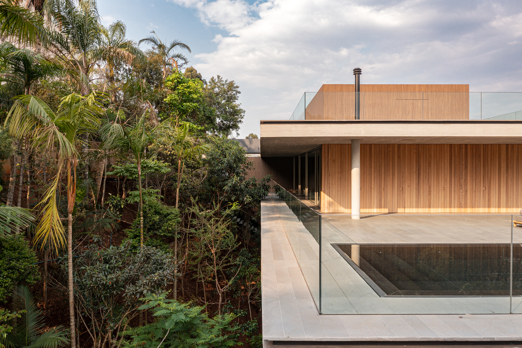 Timber clad volume with cantilevered overhang and glass balustrade adjacent to lush hillside vegetation