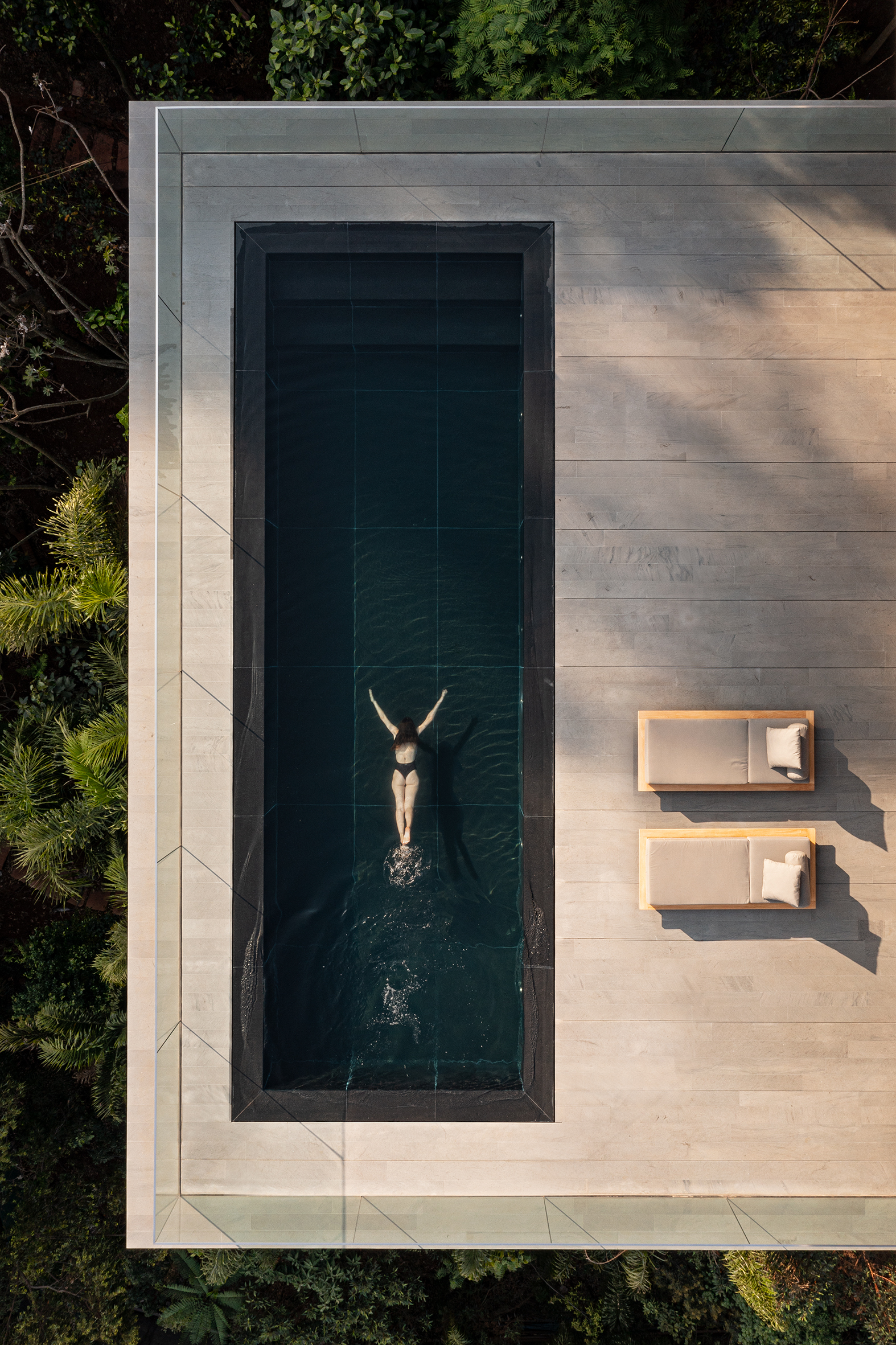 Aerial view of lap pool with swimmer and two lounge chairs on limestone paving
