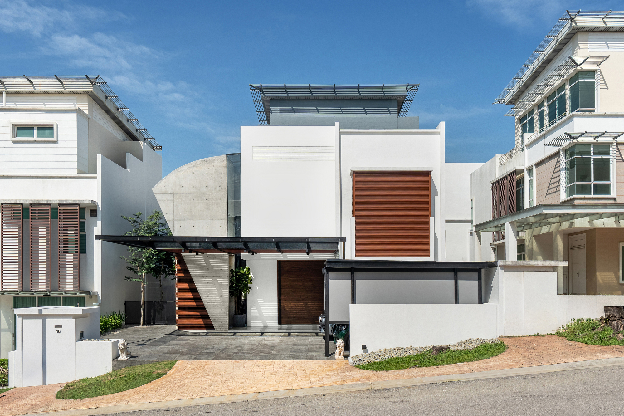 Street view of white stucco volumes with timber panels and a cantilevered canopy under a blue sky