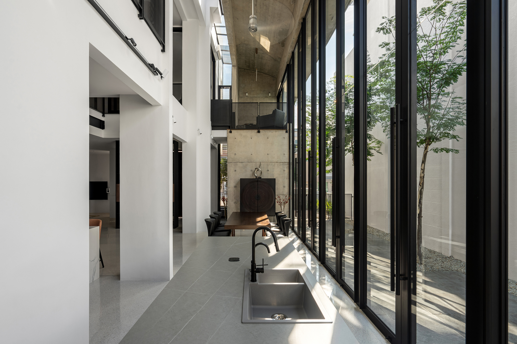 Interior corridor with terrazzo floor and folding glazed doors opening to a planted courtyard in sunlight