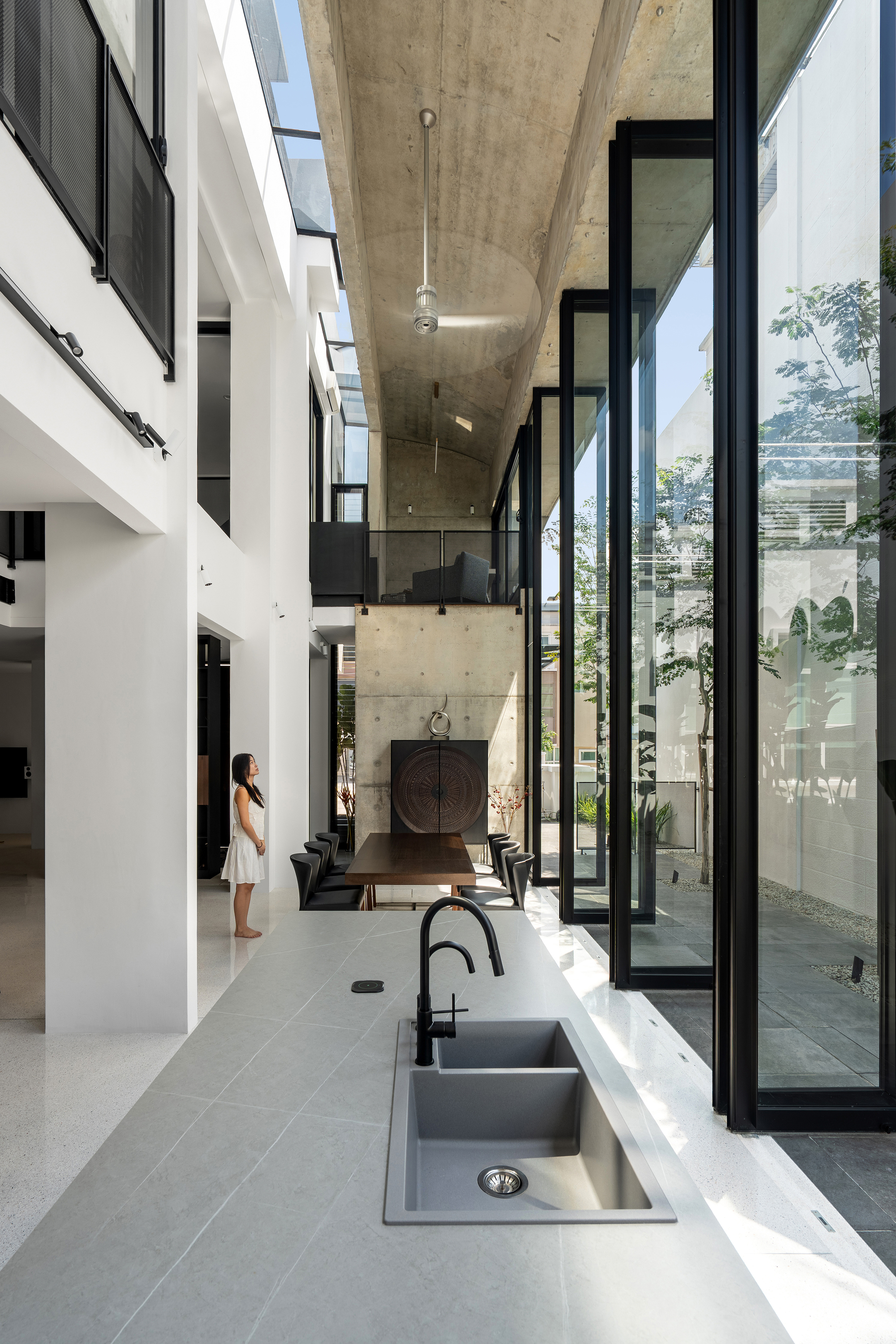 White kitchen counter with integrated sink overlooking double-height courtyard with exposed concrete ceiling and clerestory windows