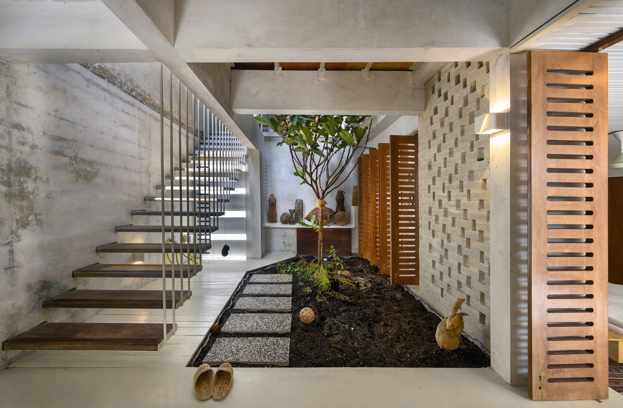 Entry foyer with cantilevered concrete staircase, central tree in planted bed, and slatted timber screens