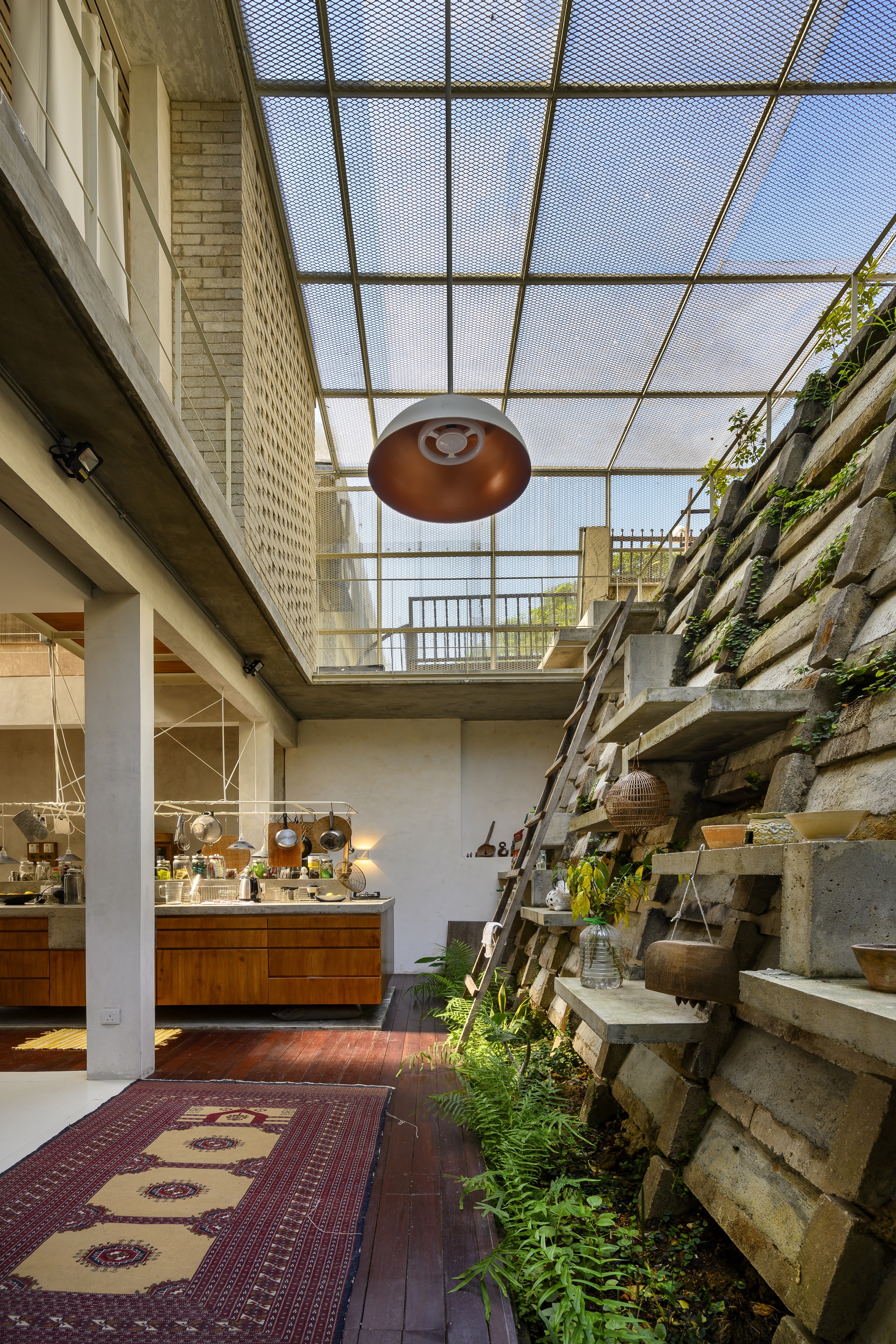Double-height living space with mesh skylight, copper pendant, and terraced concrete block planter wall