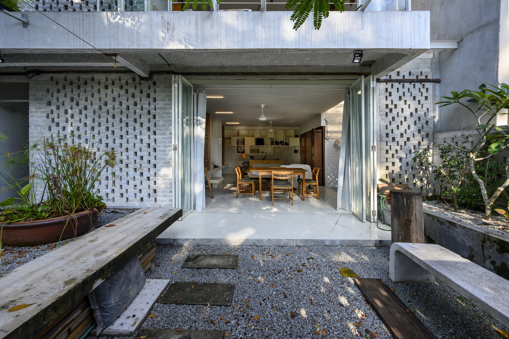 Ground-level courtyard opening to dining room through folding glass doors with gravel garden and concrete benches