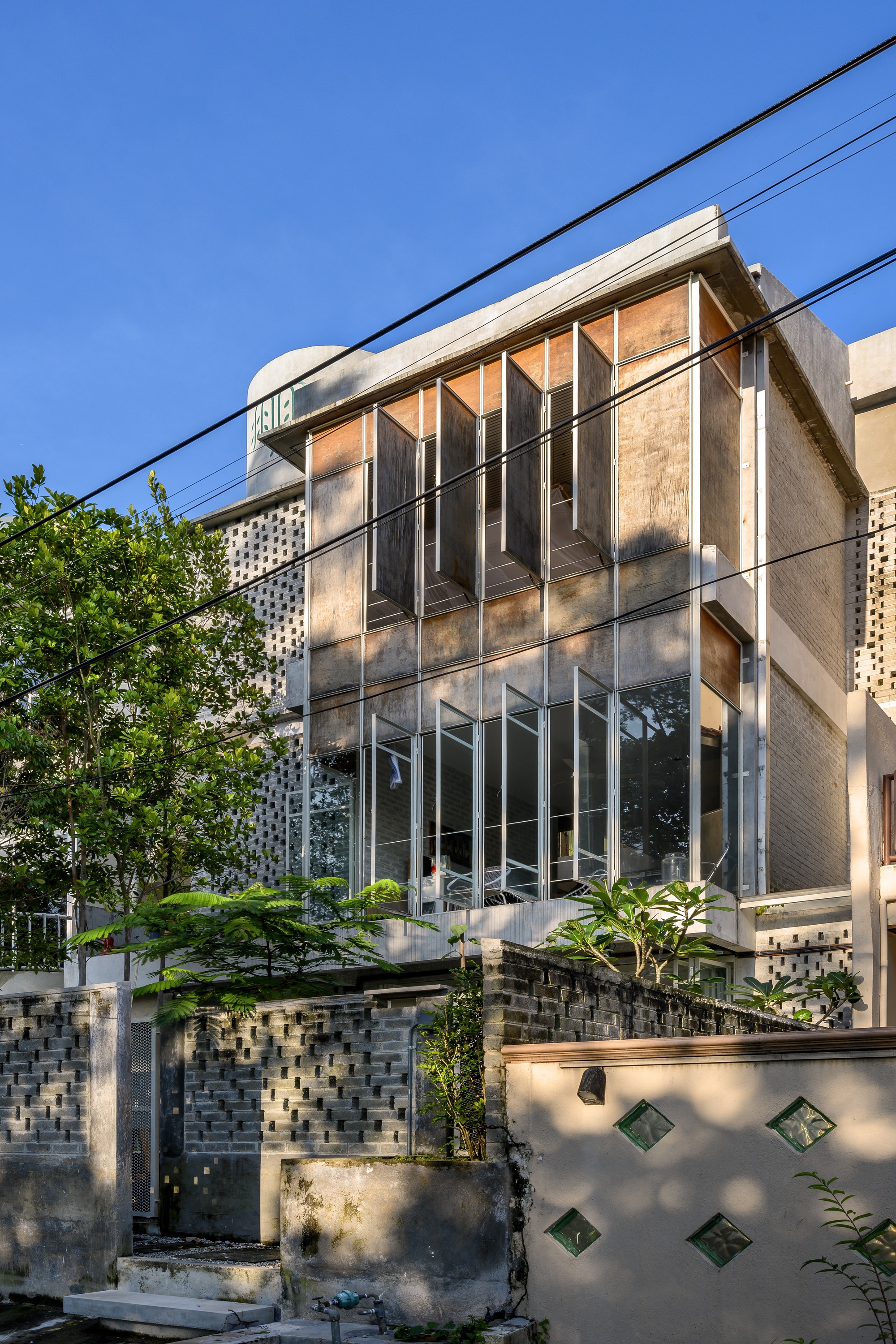 Street facade with layered corrugated metal screens, perforated brick base wall, and overhead power lines