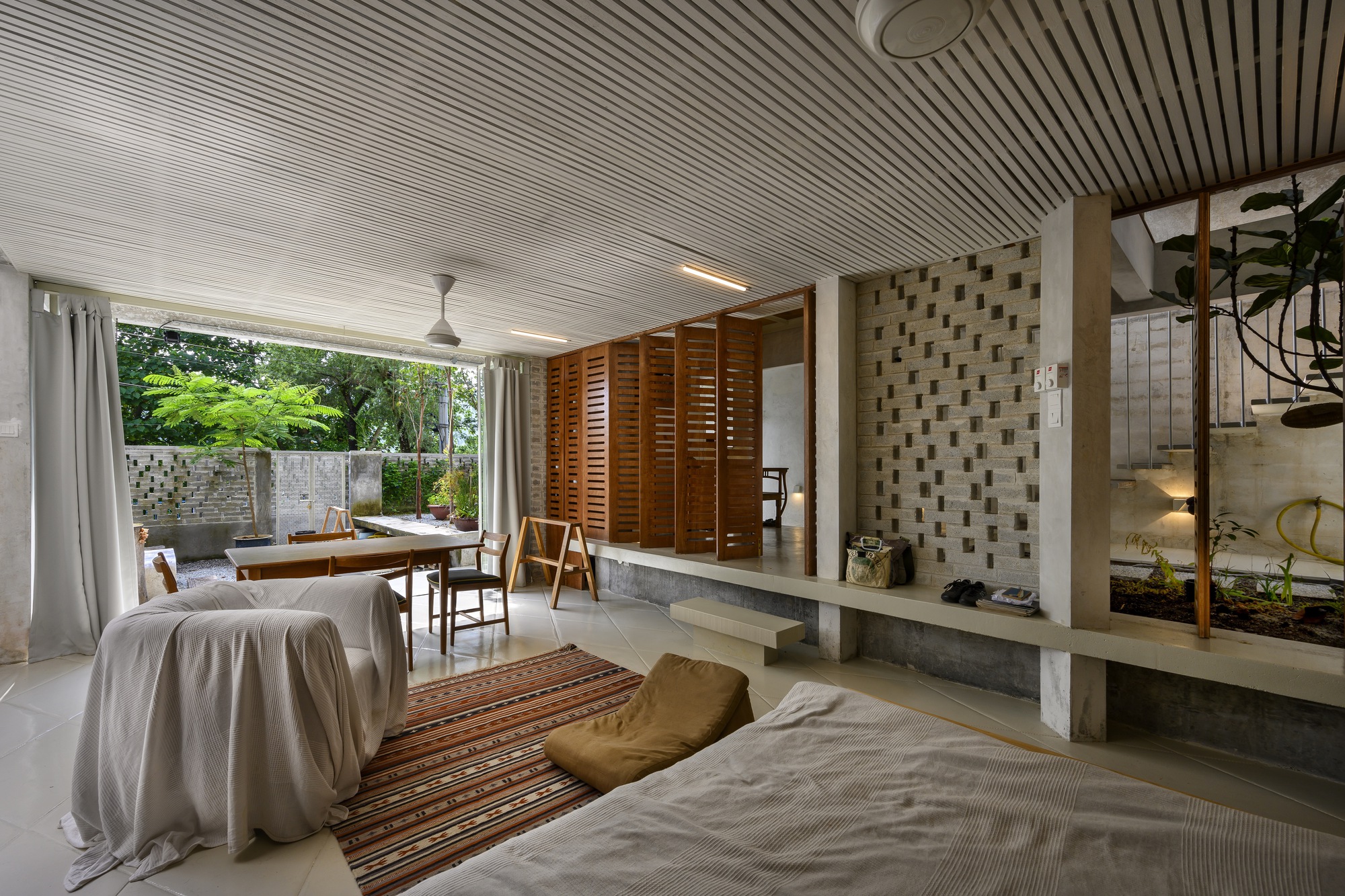 Living area with slatted ceiling opening to a planted terrace framed by white curtains