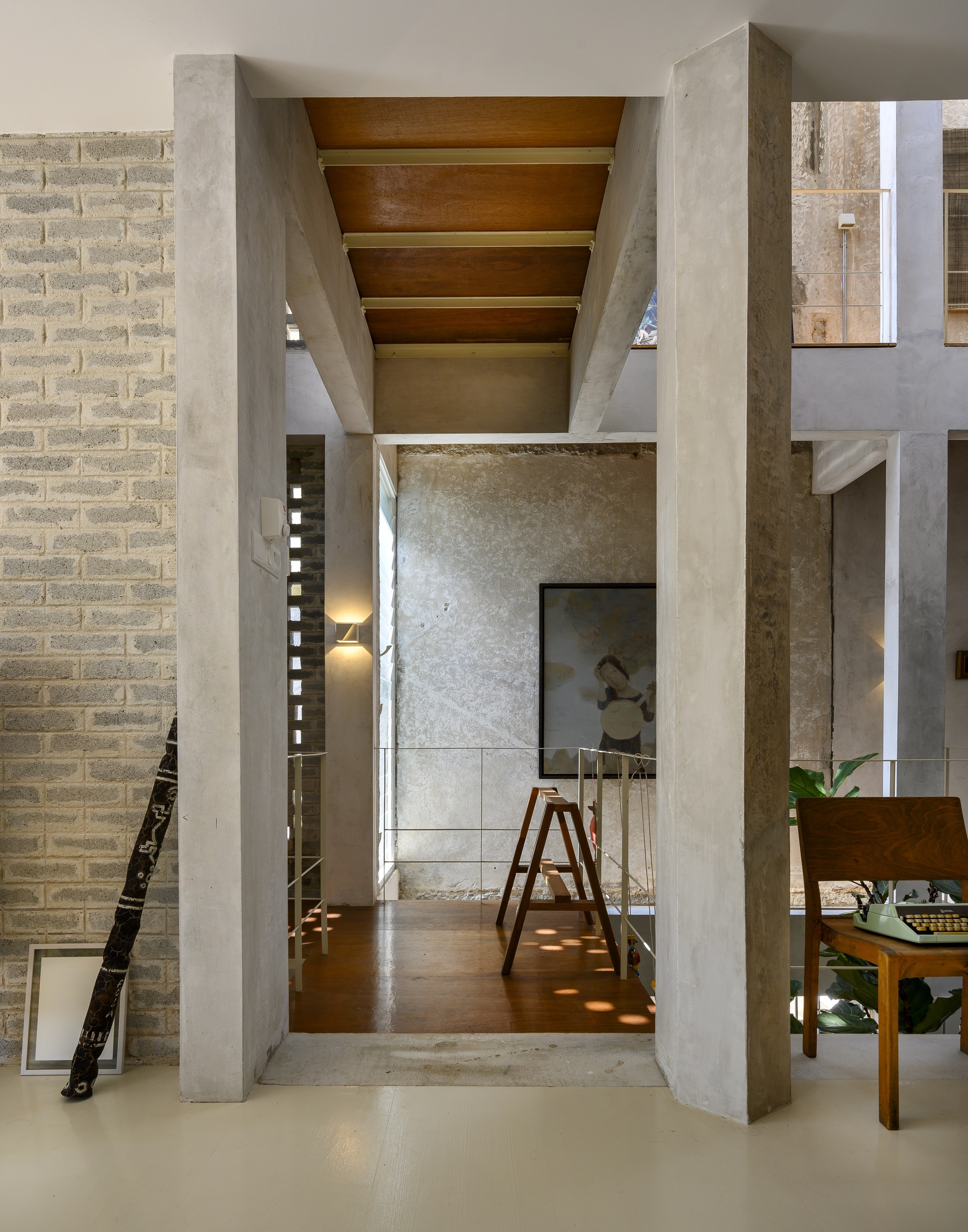Concrete portal framing a view through interconnected rooms with timber ceiling beams and warm afternoon light
