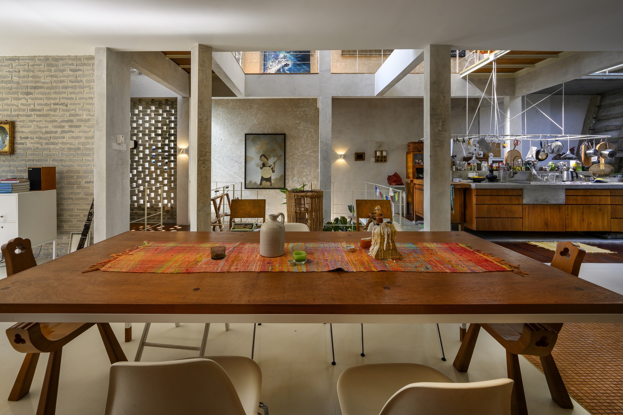Dining table beneath exposed concrete beams and clerestory windows with perforated brick wall at left