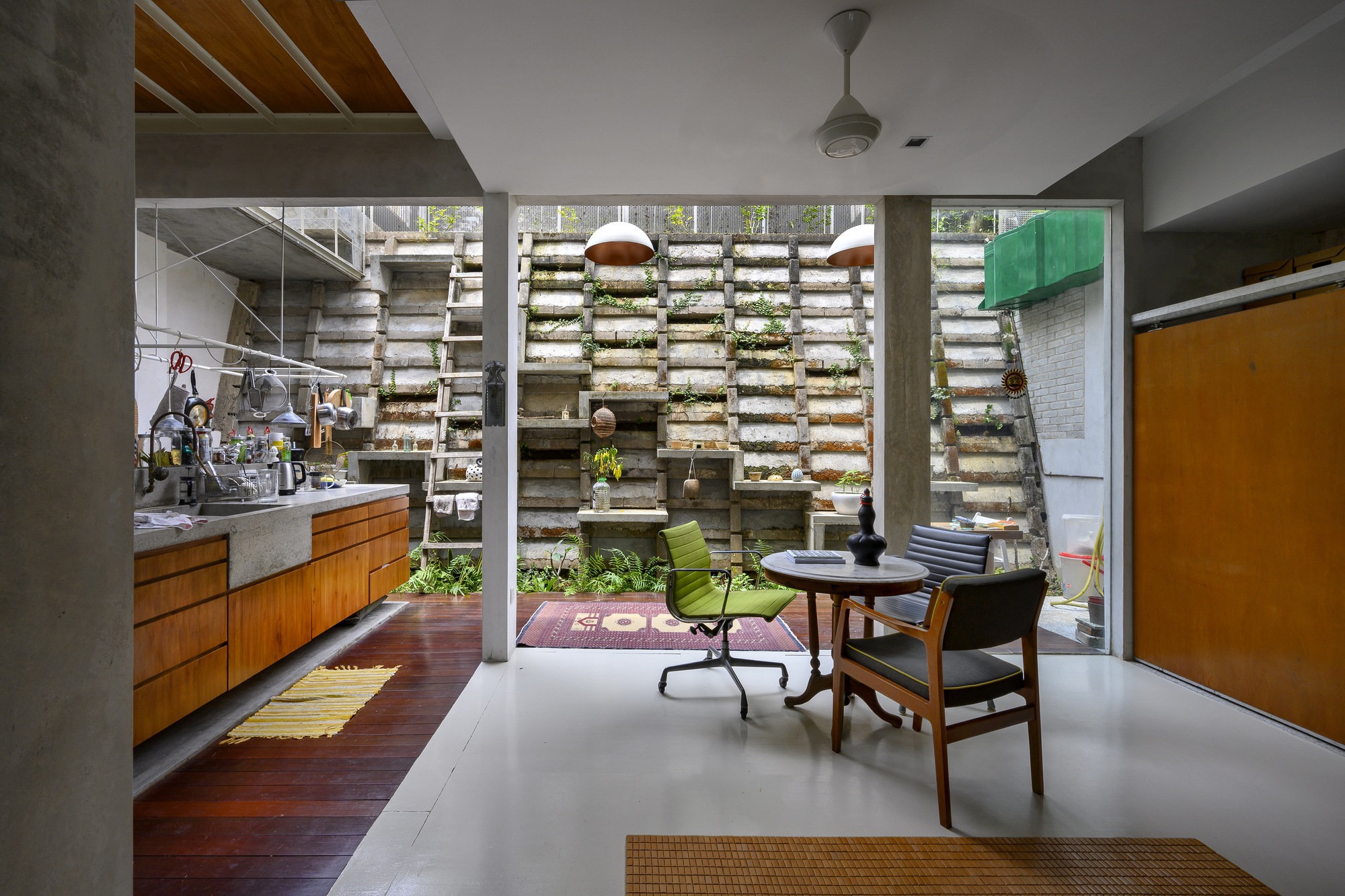 Living space opening to internal courtyard through concrete frame with horizontal louvered planting wall beyond