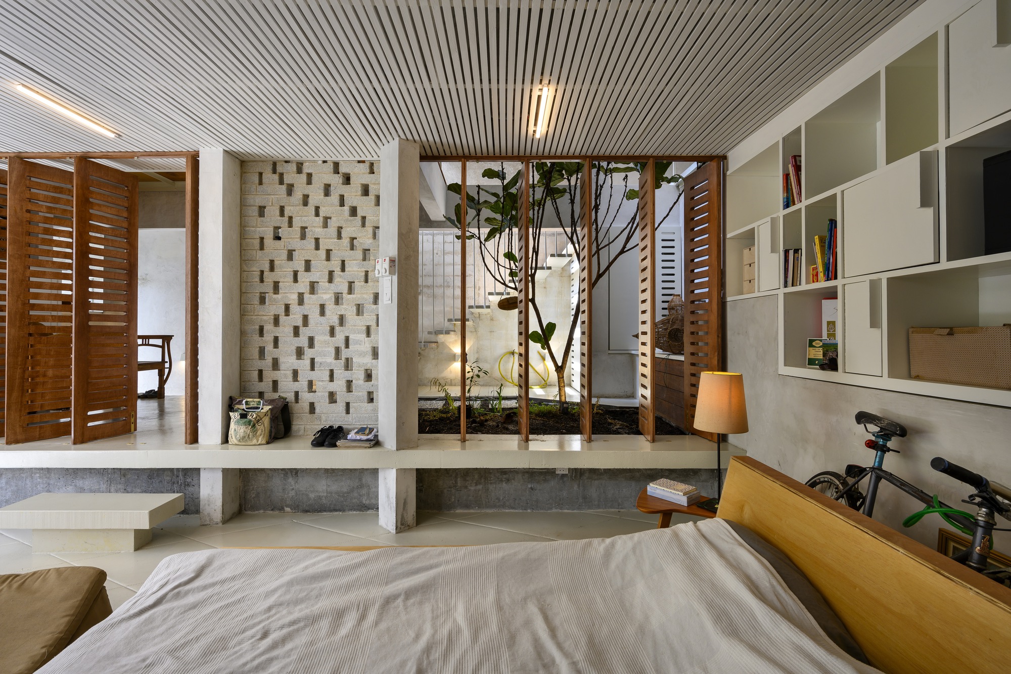 Bedroom with timber slatted ceiling, interior planted courtyard, and white shelving with louvered timber screens