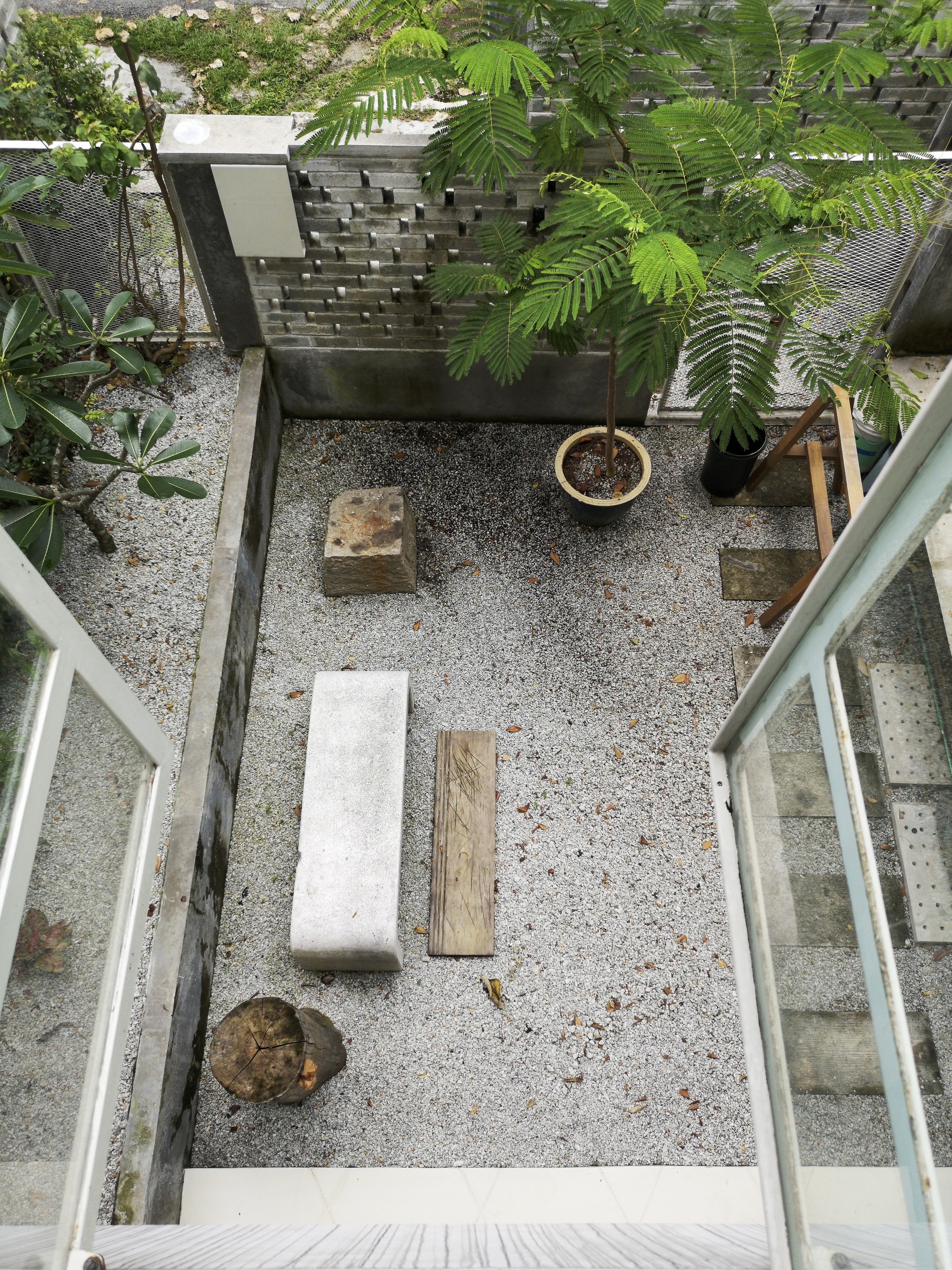 Top-down view of gravel courtyard with concrete benches, potted plants, and projecting brick wall