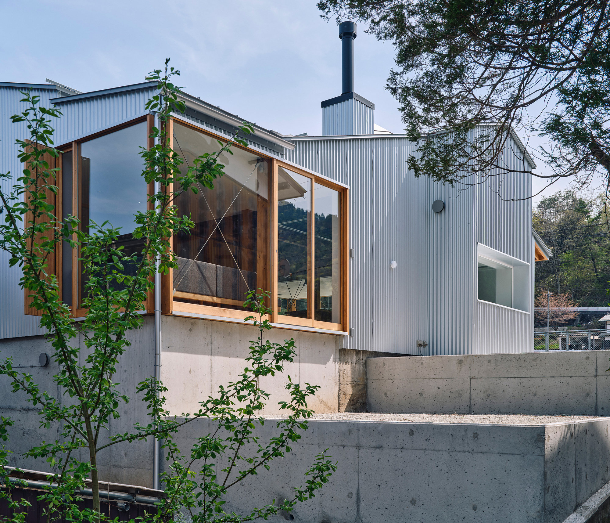 Exterior view of corrugated metal cladding and timber-framed glazing above a concrete base with young trees