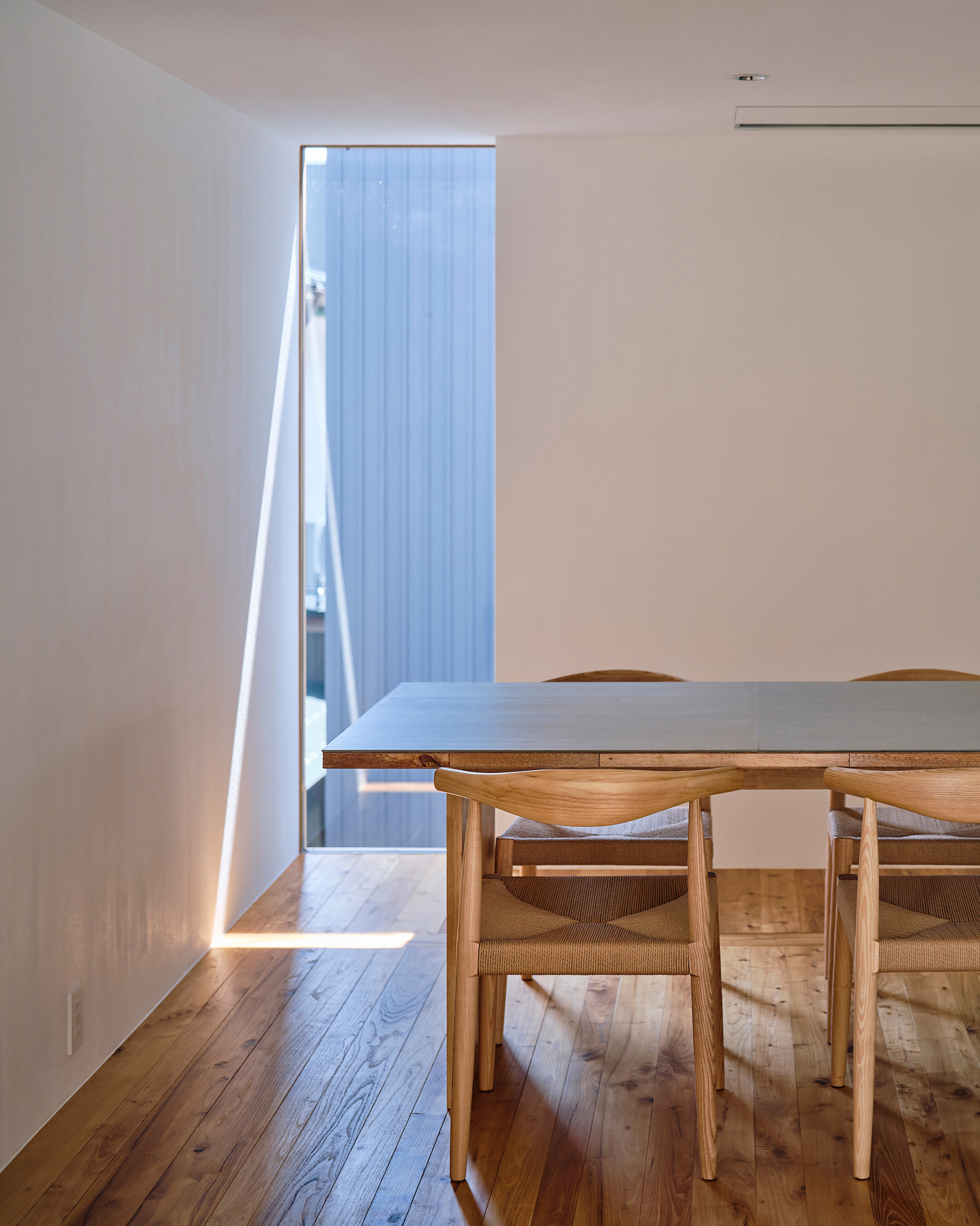 Narrow door opening with sunlight streaming across timber flooring toward a dining table