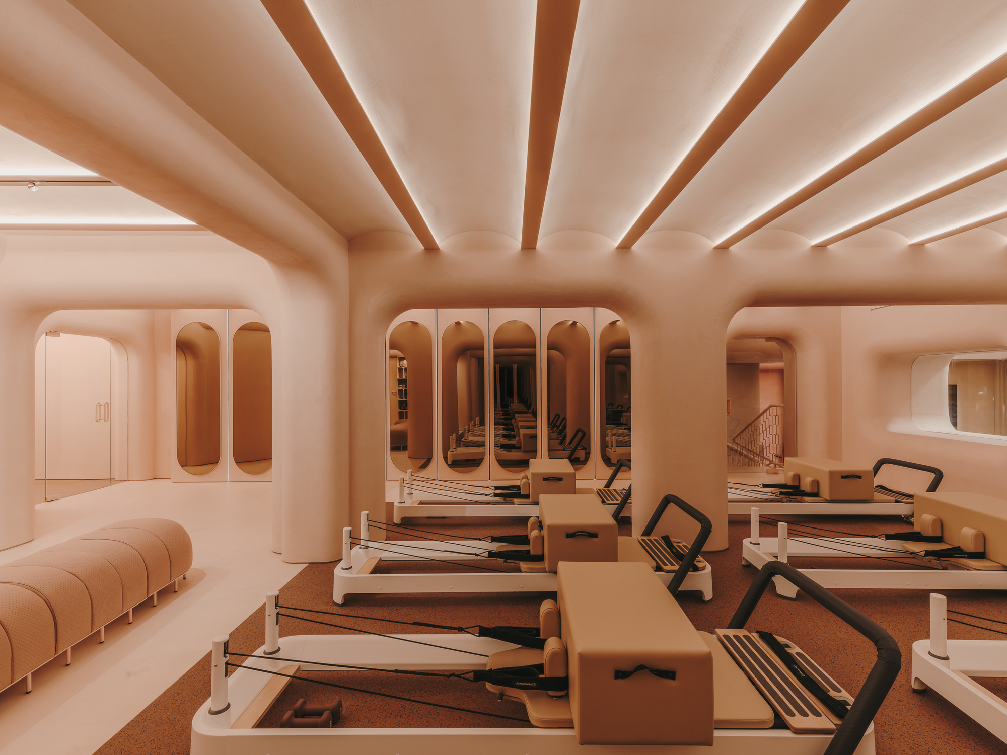 Pilates studio with rows of reformer equipment beneath arched openings and ribbed ceiling beams with uplighting