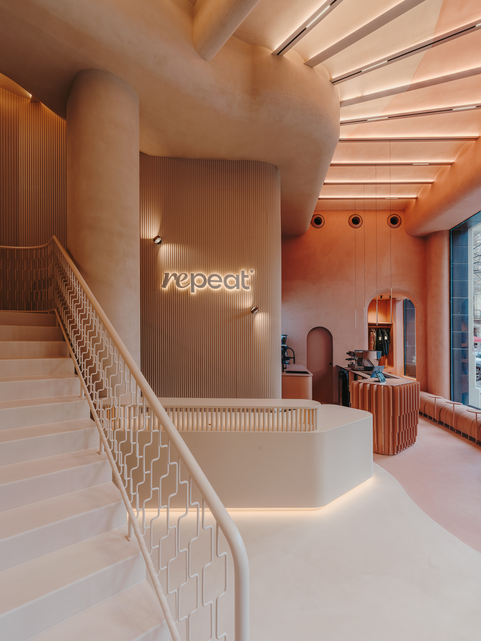 Reception desk with illuminated signage beneath a curved staircase with geometric balustrade and slatted timber wall