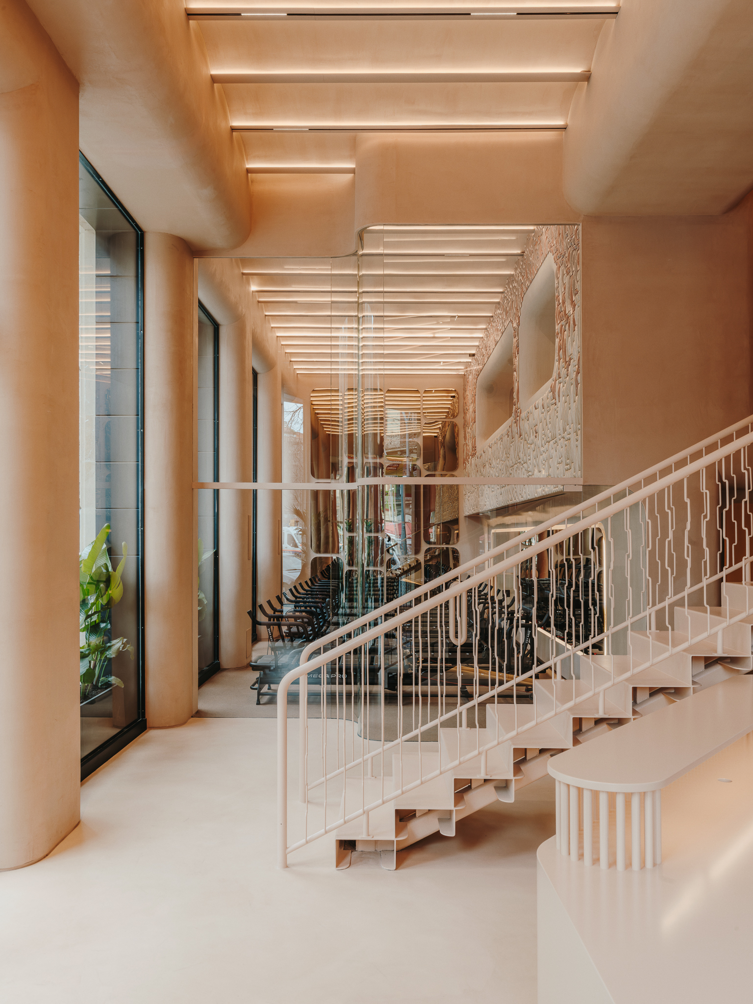 Double-height lobby with floating staircase and linear ceiling baffles overlooking potted plants and exercise area