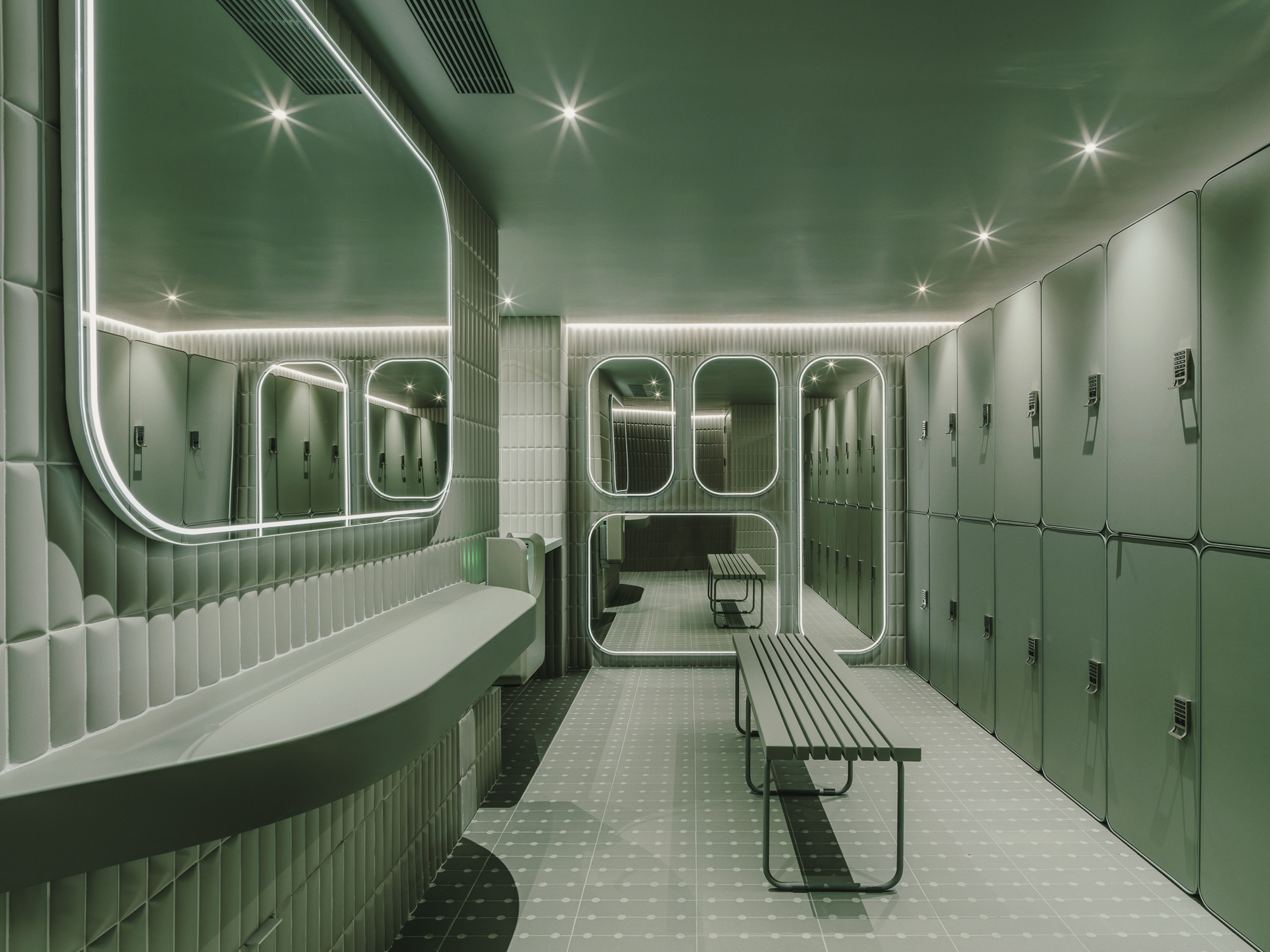Locker room with fluted green tile walls, rounded mirrors with neon lighting and metal benches