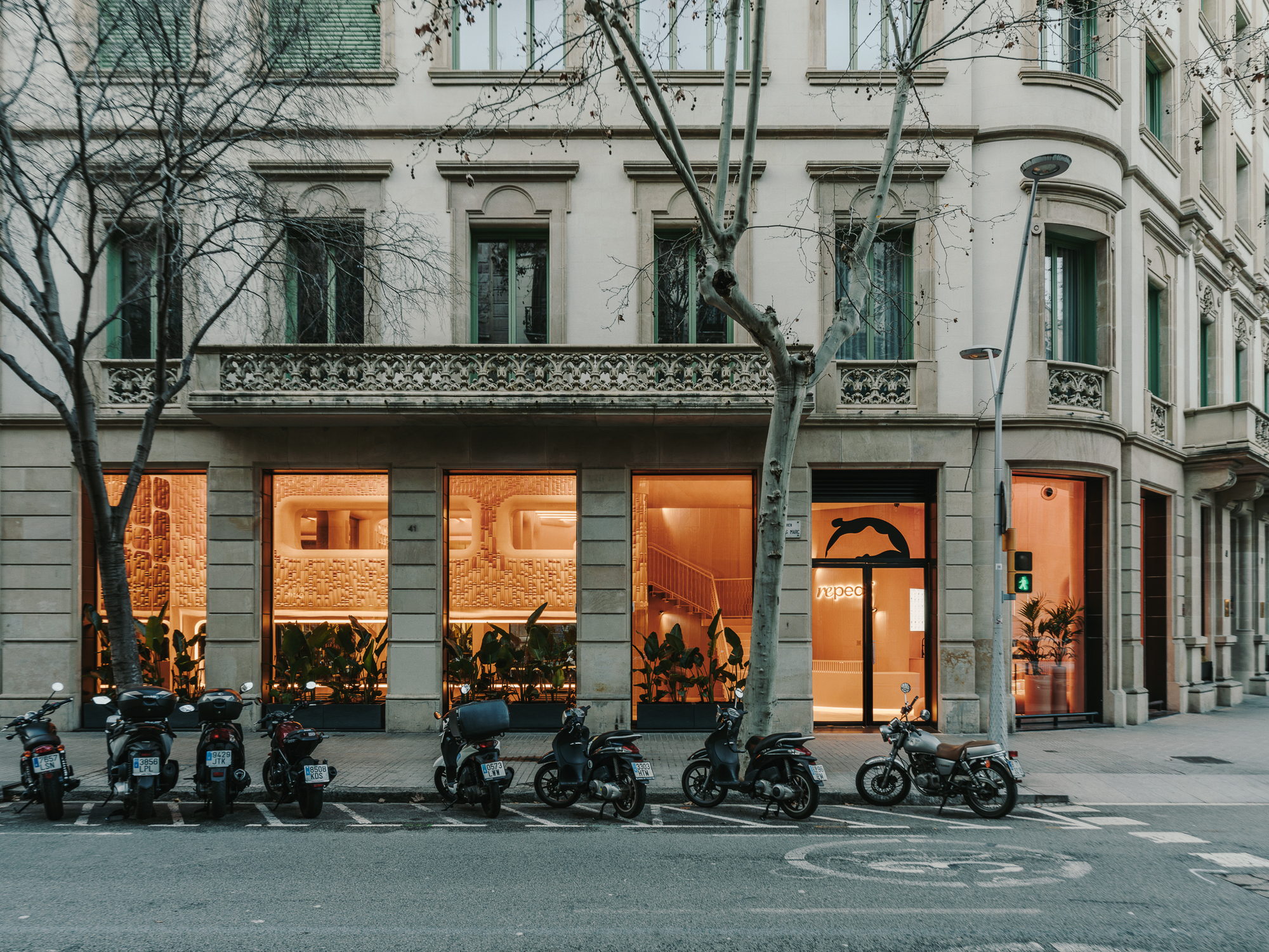 Corner storefront with illuminated interior visible through large windows at dusk with parked scooters along sidewalk